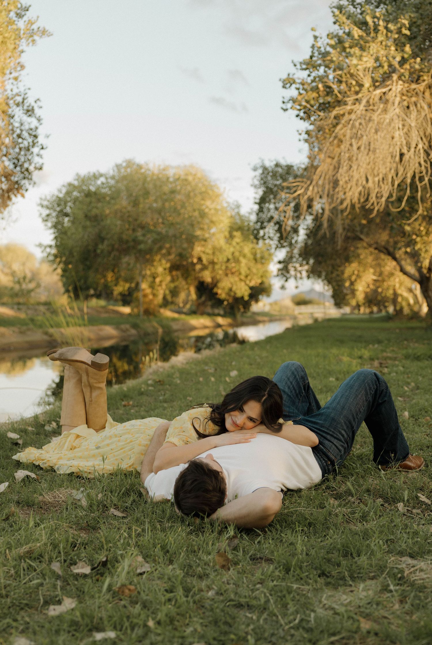 A couple lies together on grass during a warm sunset in a peaceful park setting.