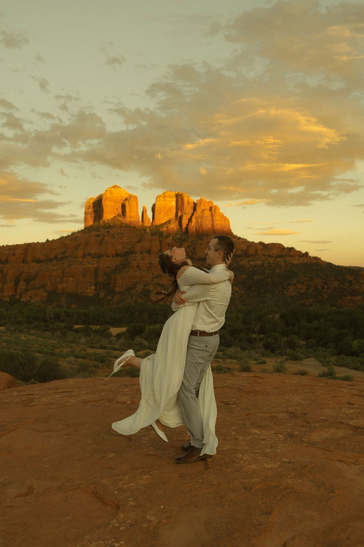 Couple embracing at sunset with Cathedral Rock in Sedona, Arizona glowing golden behind them during a romantic wedding elopement.
