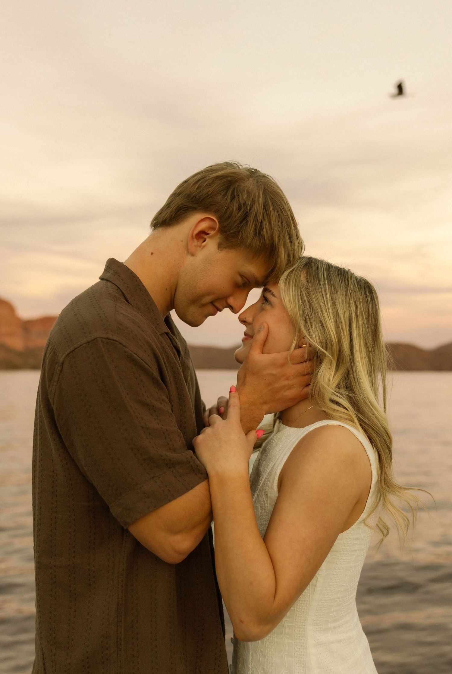 Couple embracing tenderly against a waterfront backdrop during golden hour.