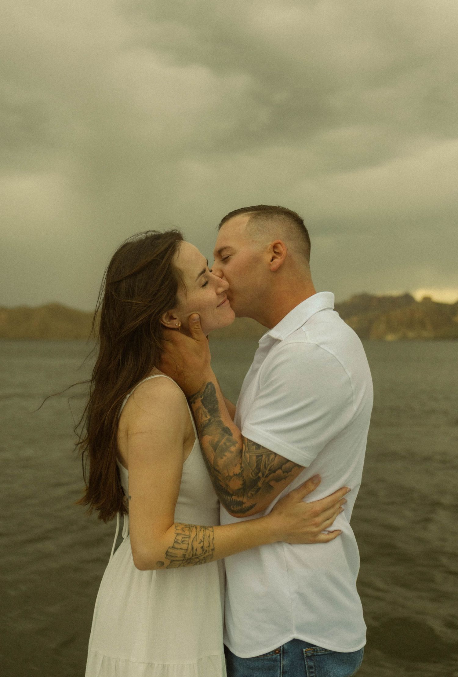 Intimate moment between couple with tattoos against moody mountain landscape.