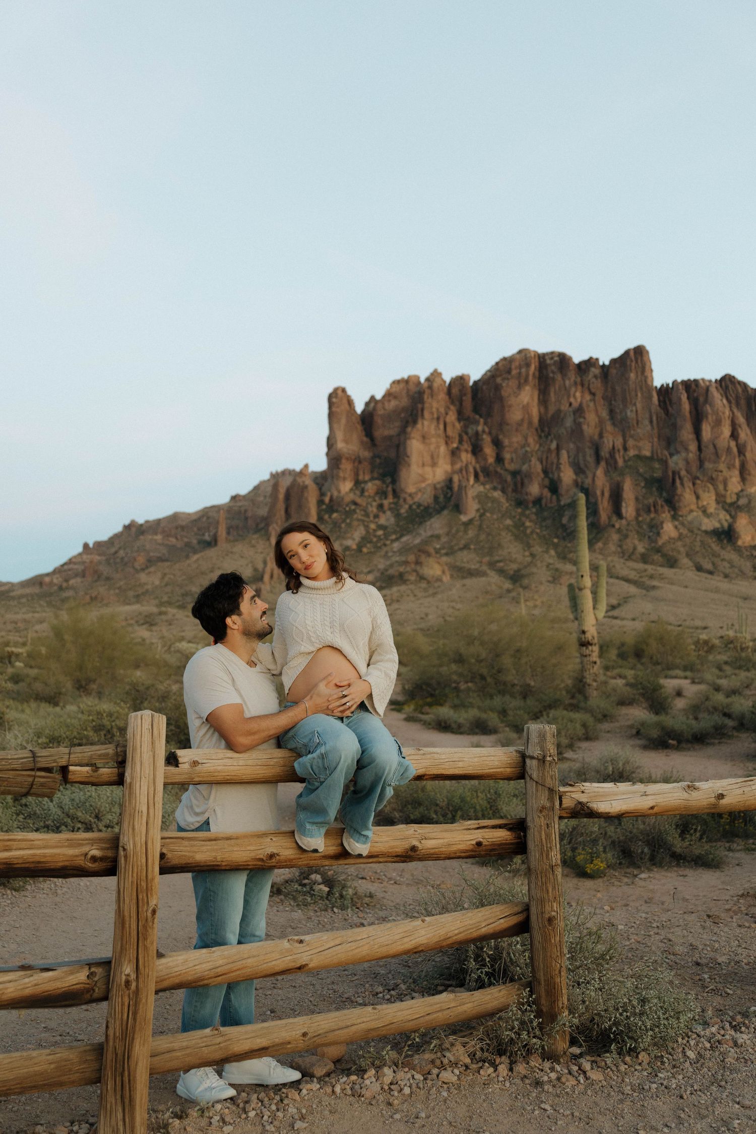 A couple shares intimate moments while sitting on a wooden fence in the desert.
