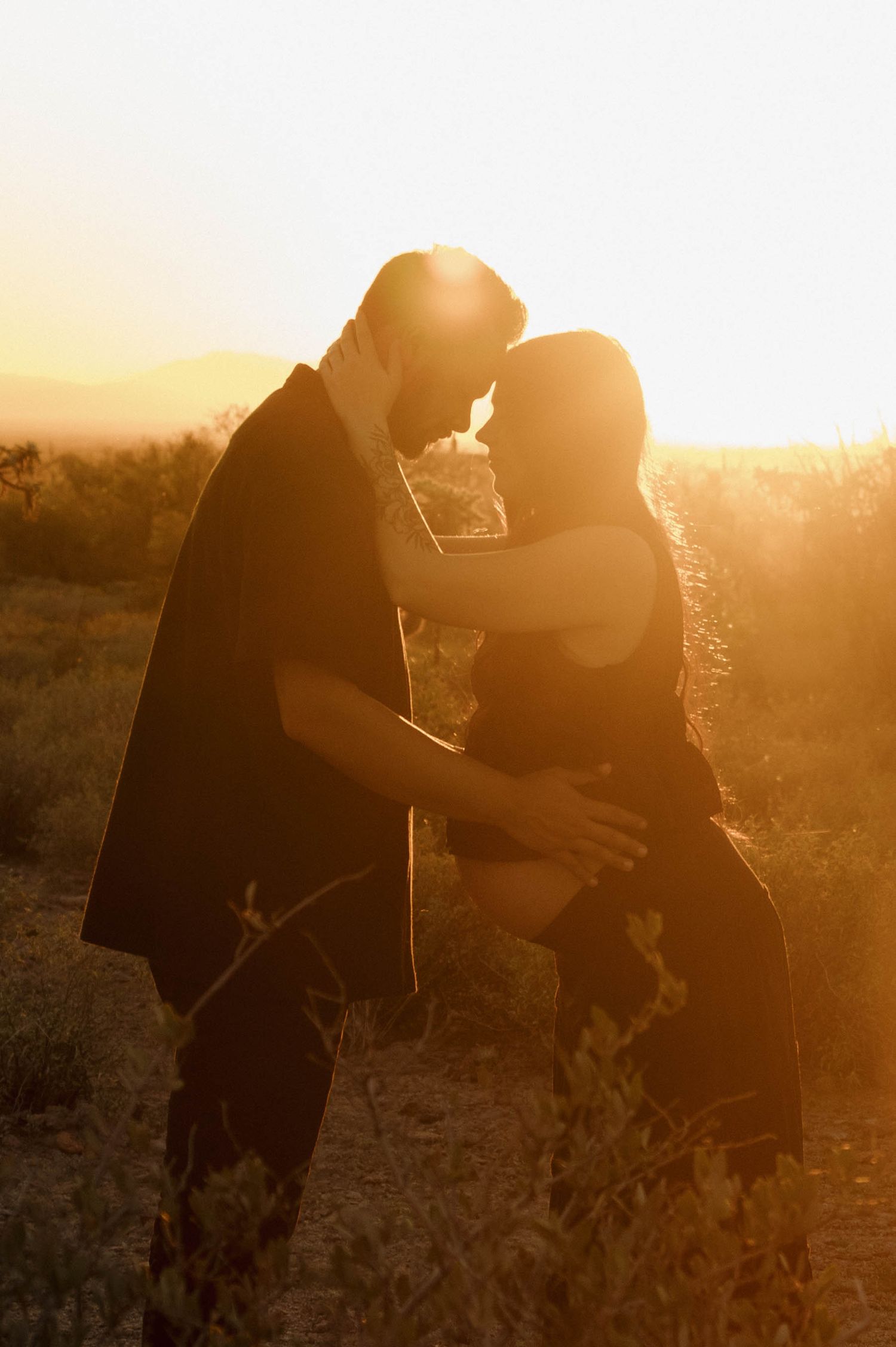 A silhouetted couple embraces in a golden sunset against a rural landscape background.