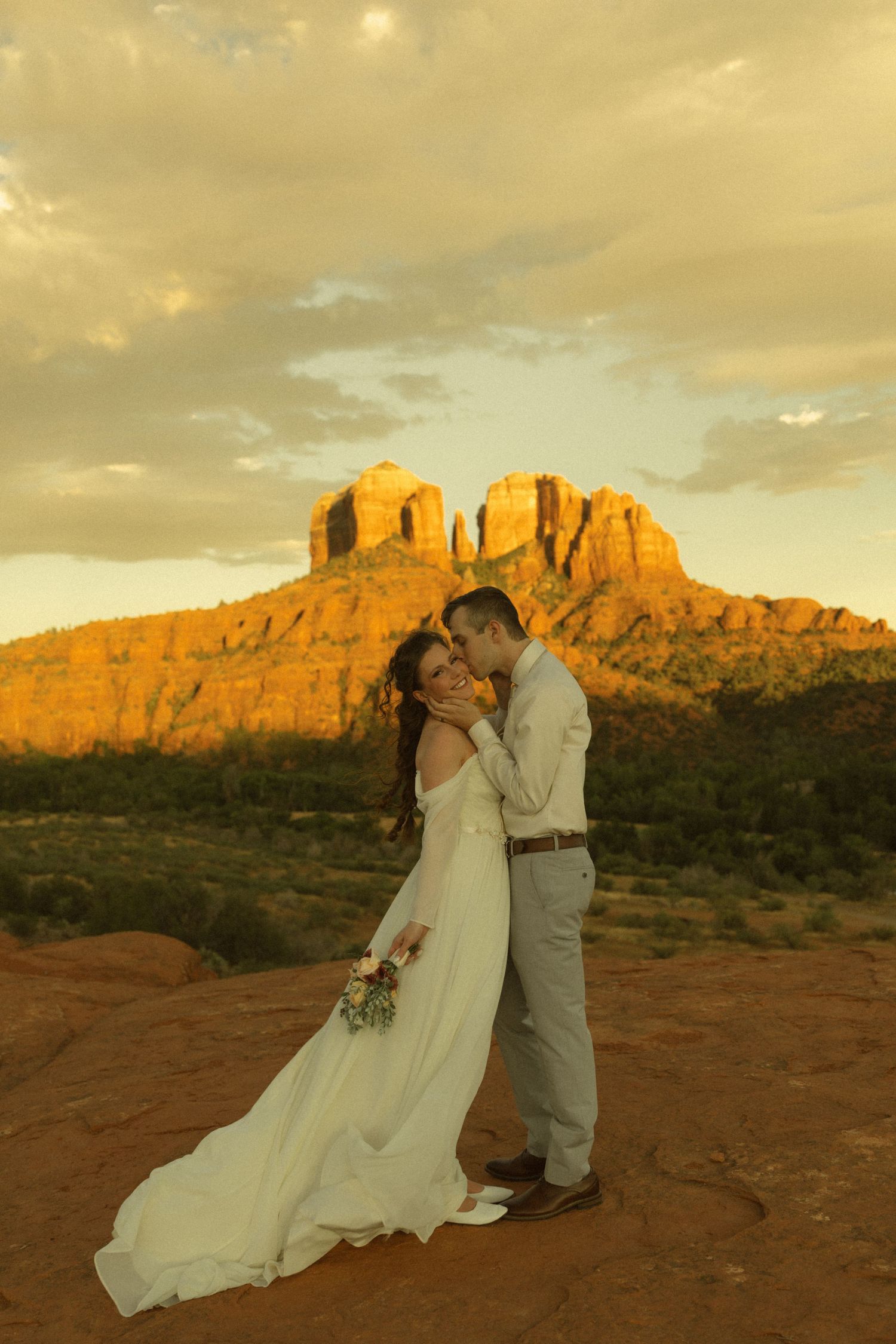 Bride and groom share a romantic moment at sunset with Cathedral Rock in Sedona, Arizona glowing golden behind them.