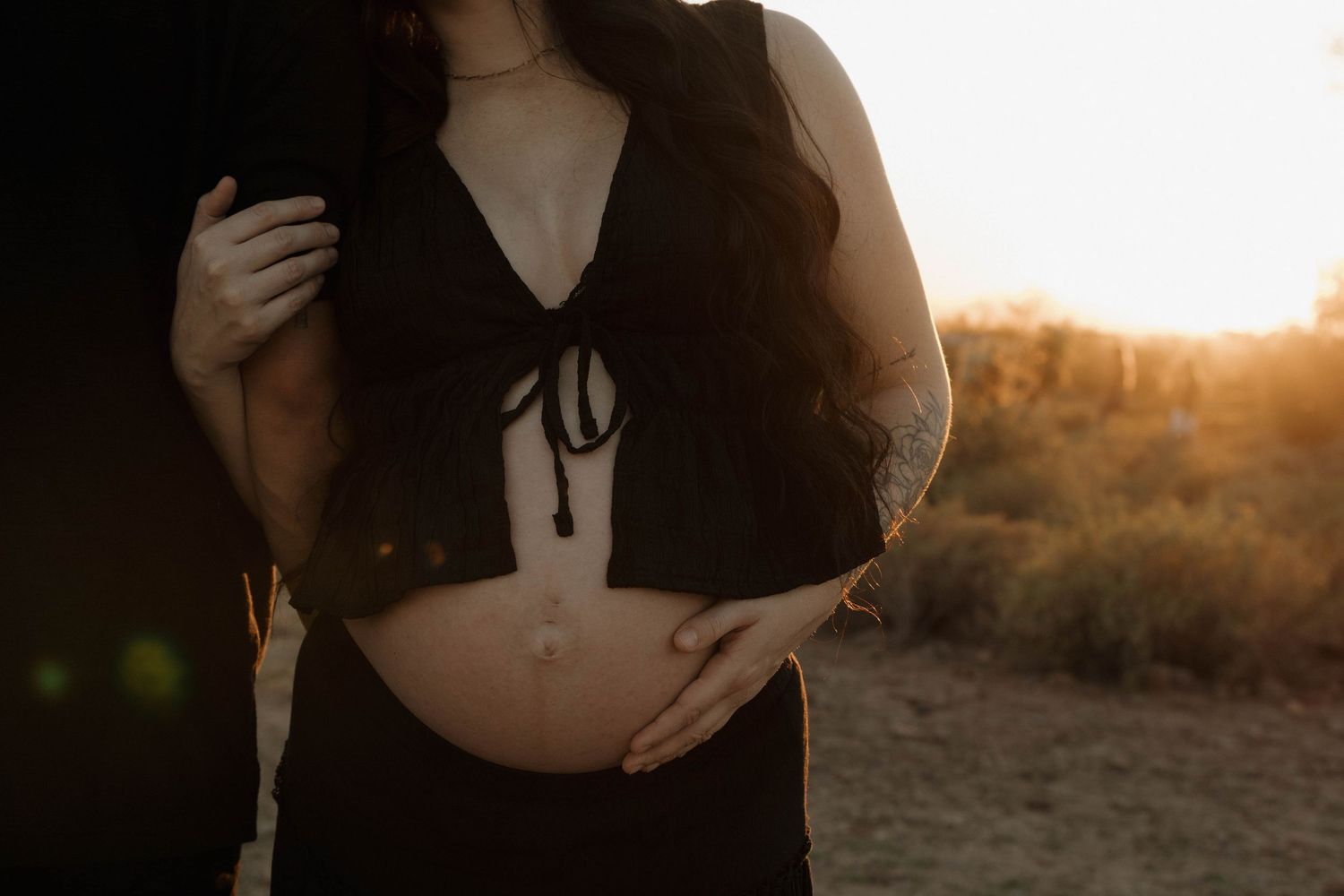 Silhouetted figure in black clothing stands against warm sunset light in outdoor setting.