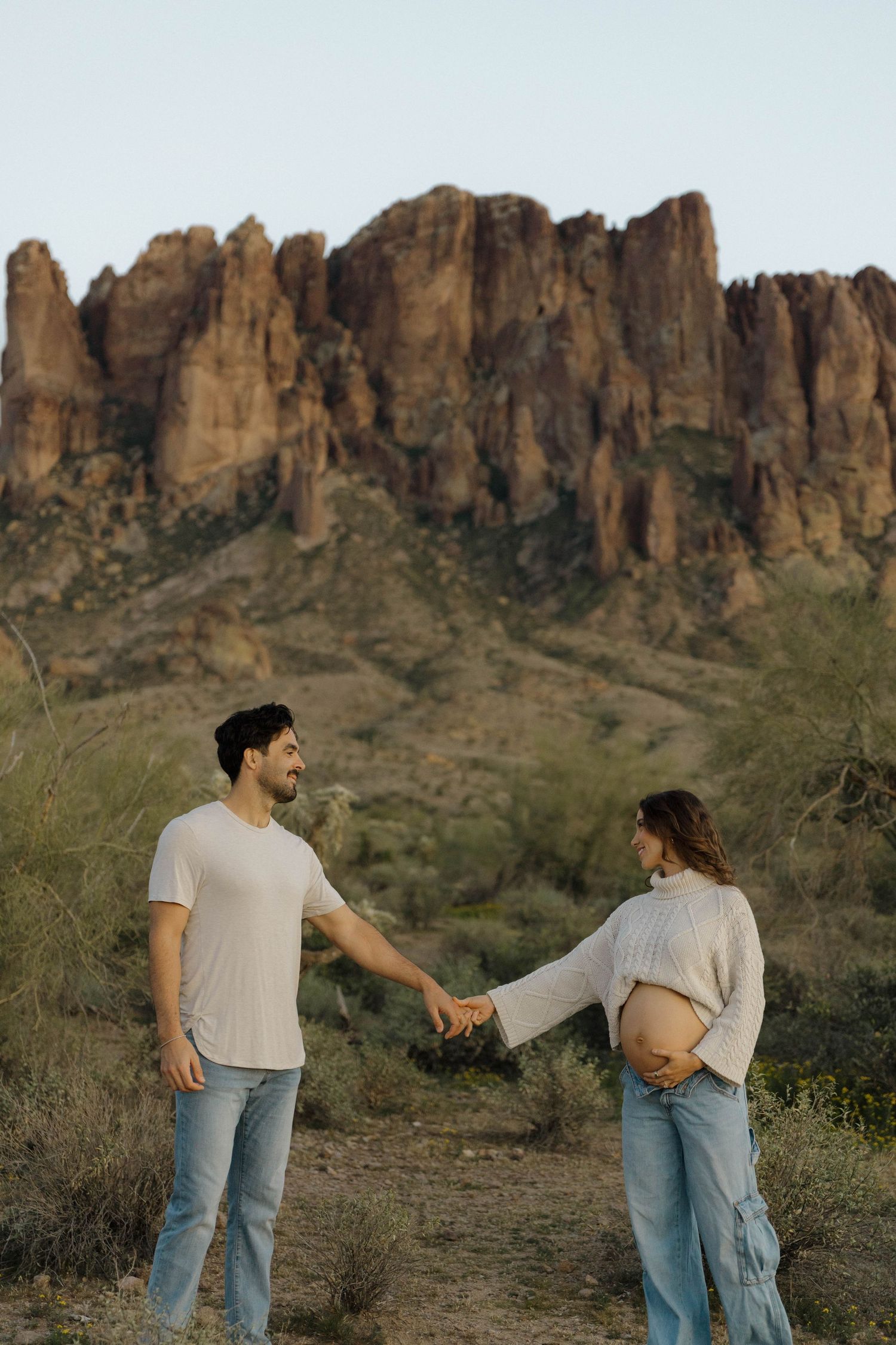 A playful maternity photoshoot with desert cliffs and cacti in the background.