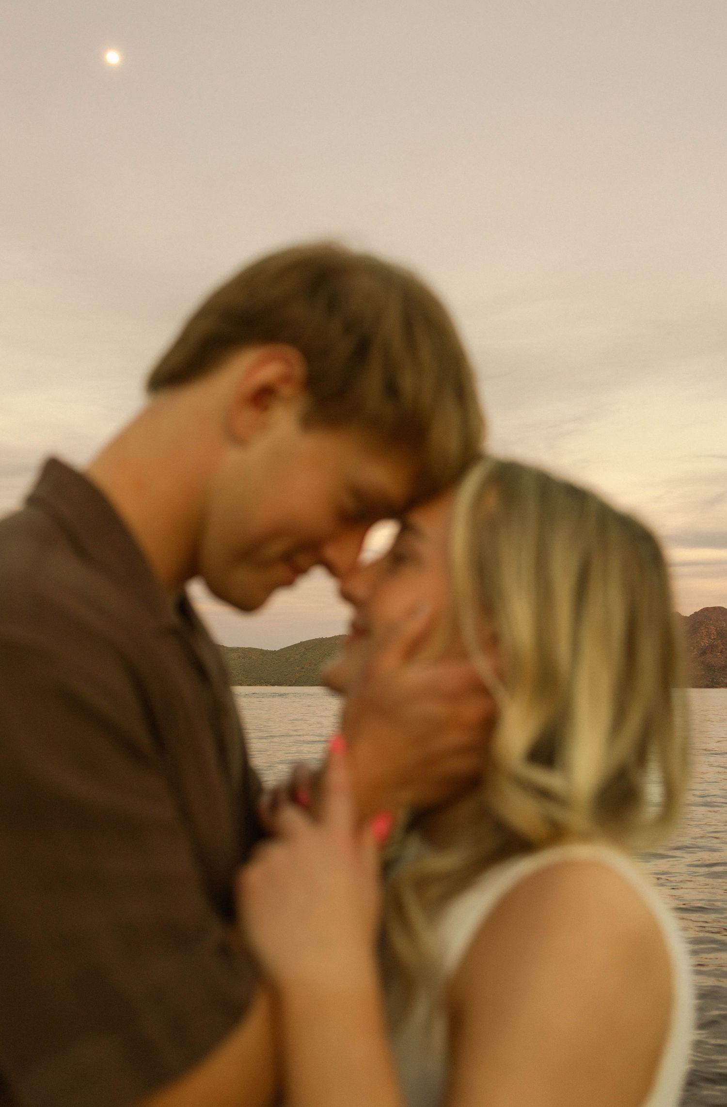 Romantic couple sharing an intimate moment at sunset by the ocean in warm lighting.