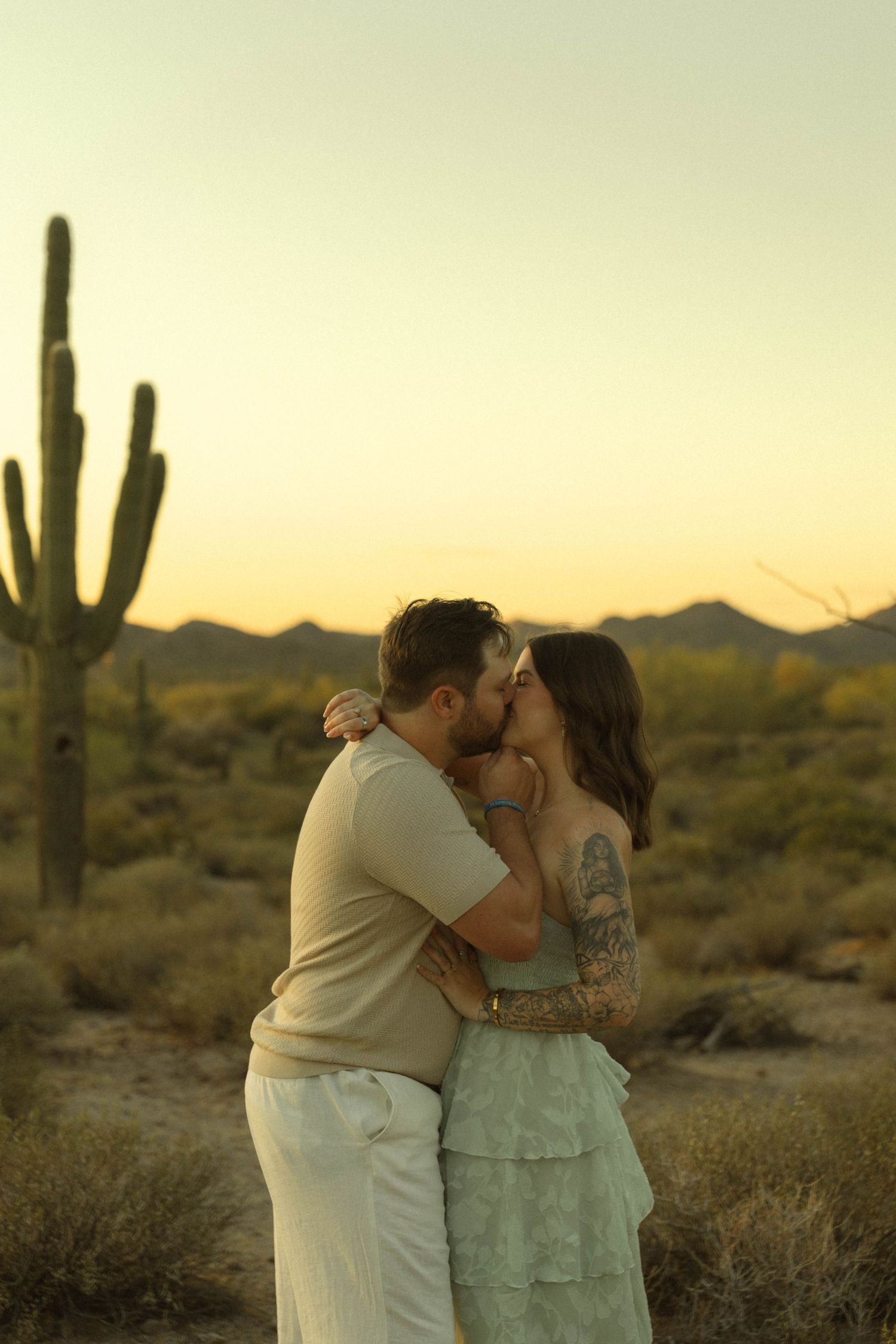 Couple sharing a kiss at sunset in the Sonoran Desert with saguaro cacti.