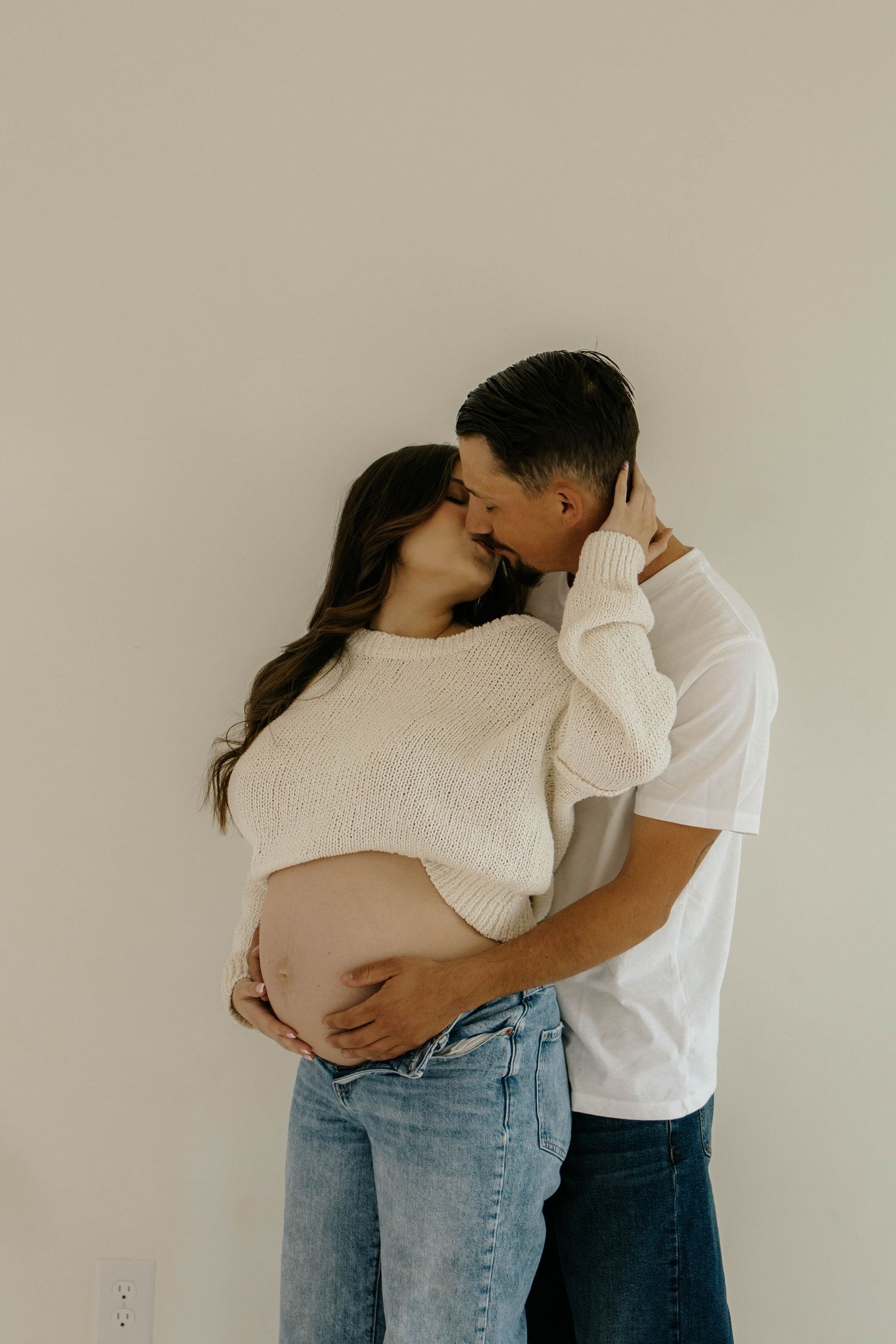 A series of minimalist romantic photos showing a couple embracing against a neutral wall background.