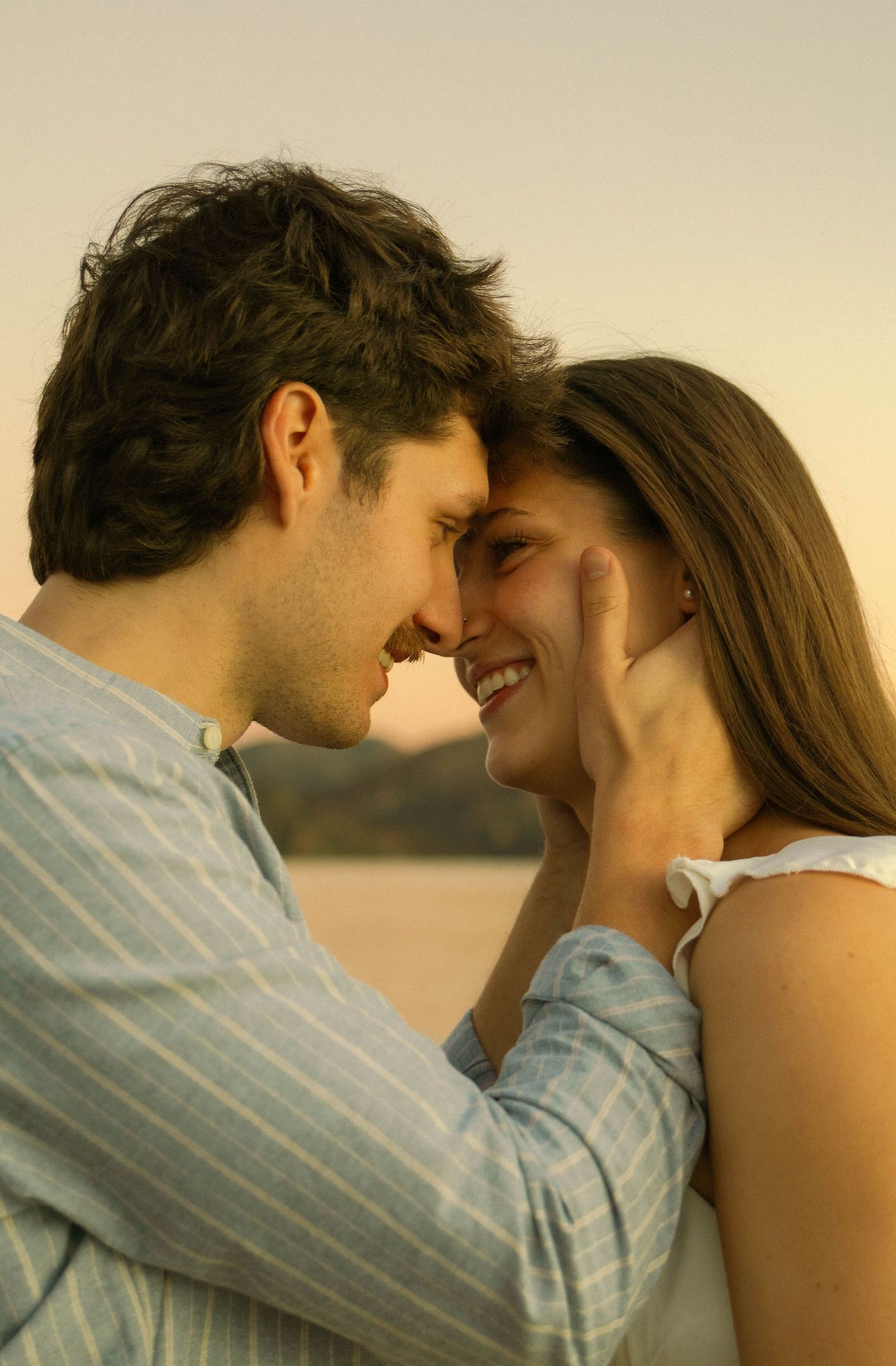 Romantic couple shares intimate moment on dock during golden hour by the water.