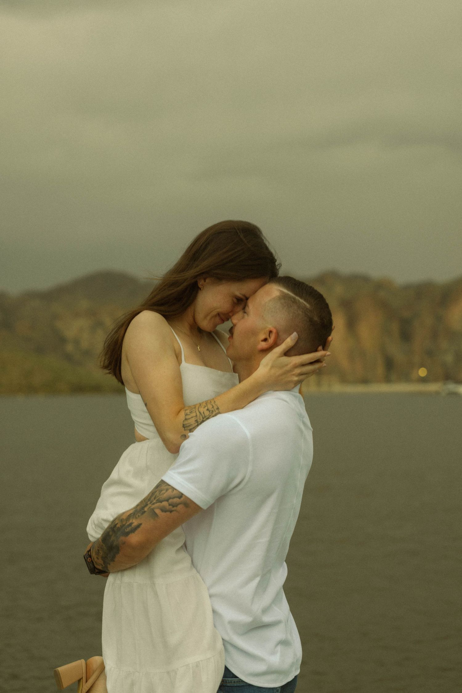 An intimate moment between a couple in white attire against a scenic mountain backdrop.