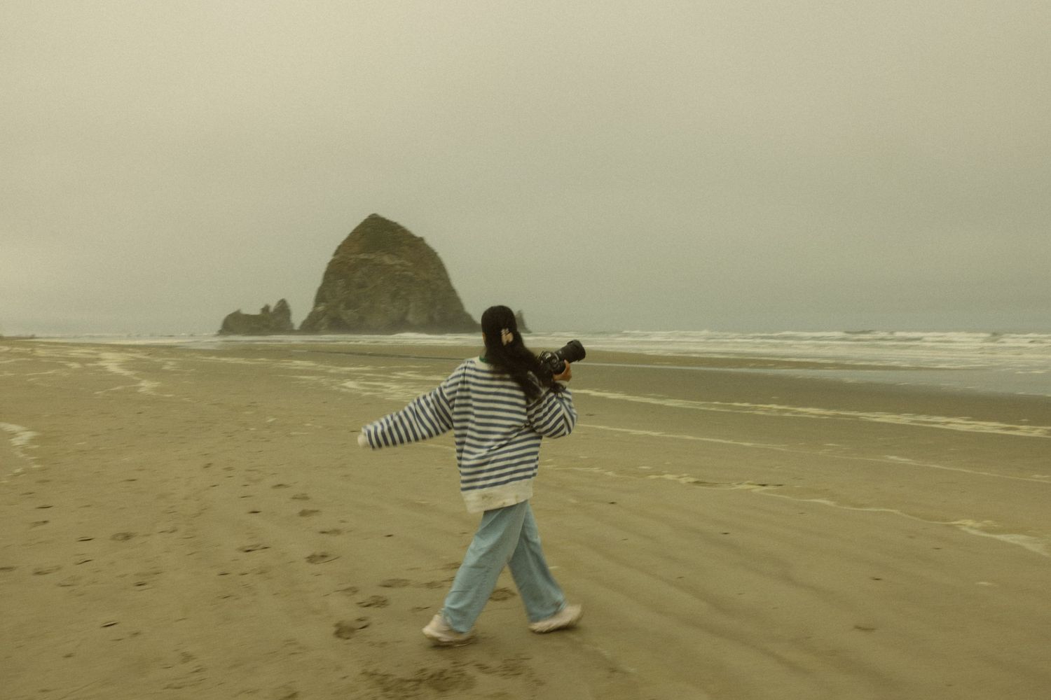 A girl walks along a foggy Oregon beach with Haystack Rock in the background at Cannon Beach.