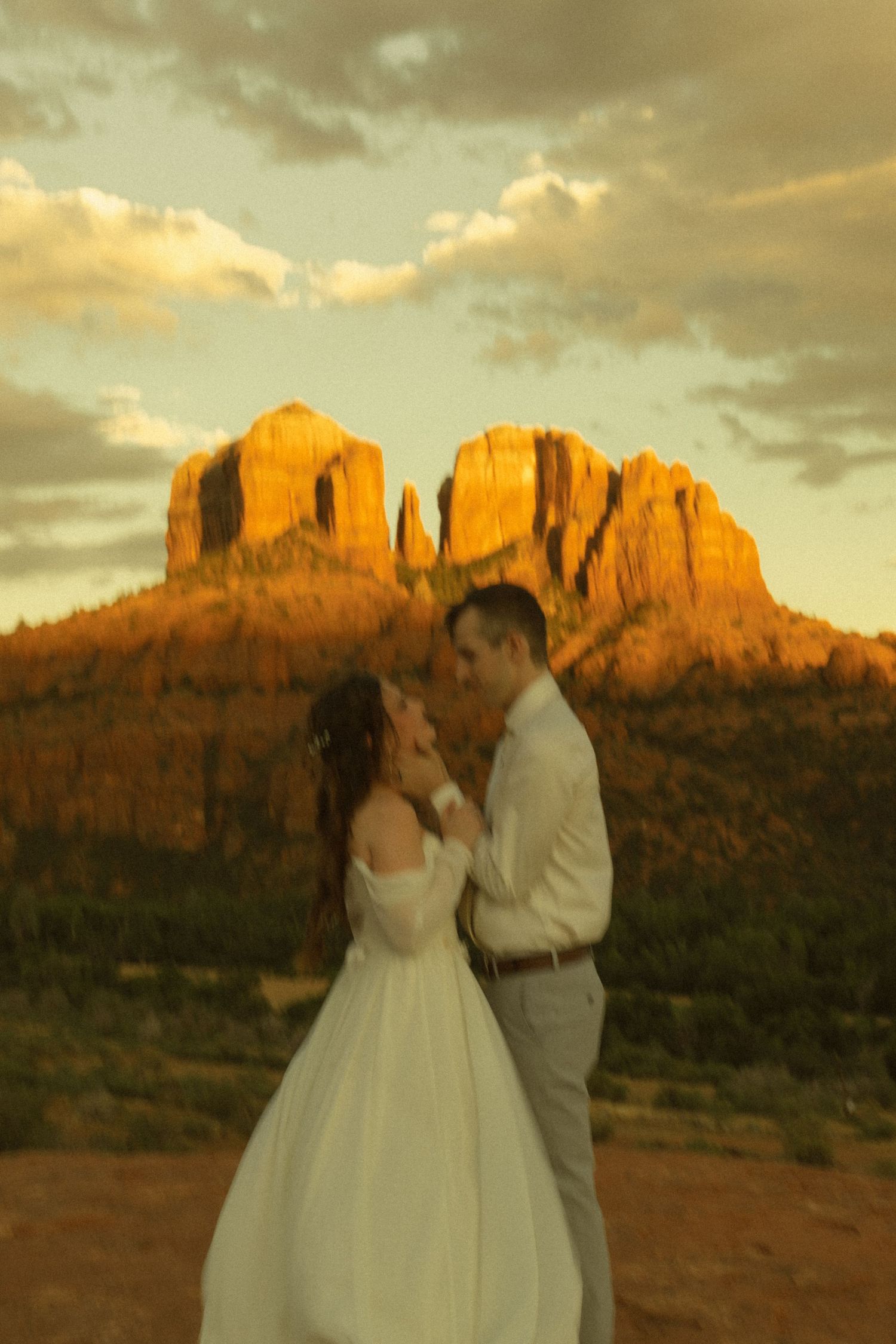 Couple in wedding attire sharing a romantic moment at sunset with Cathedral Rock in Sedona, Arizona glowing golden behind them.