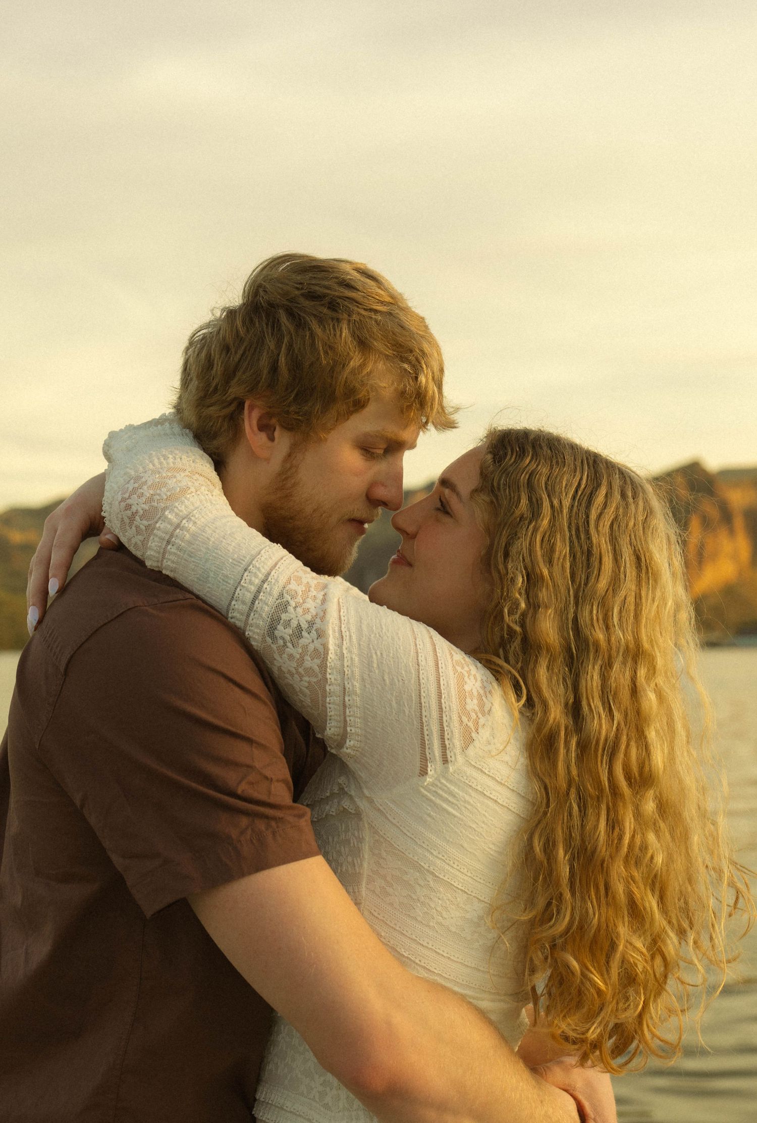 Tender moment between lovers during sunset near a serene waterfront.