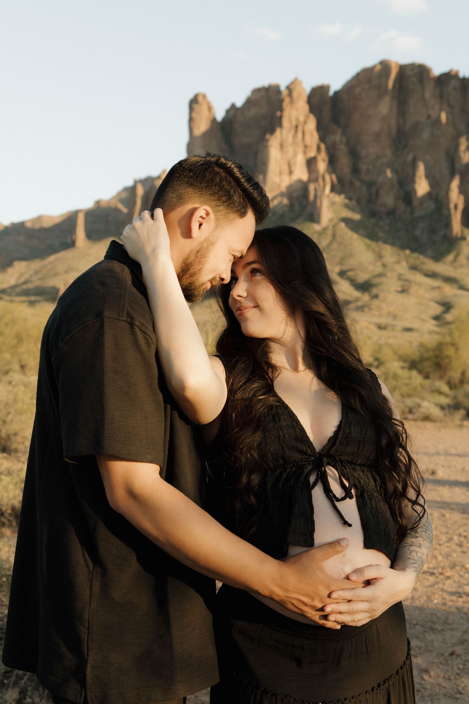 An intimate couple embraces against the backdrop of towering desert cliffs at sunset.