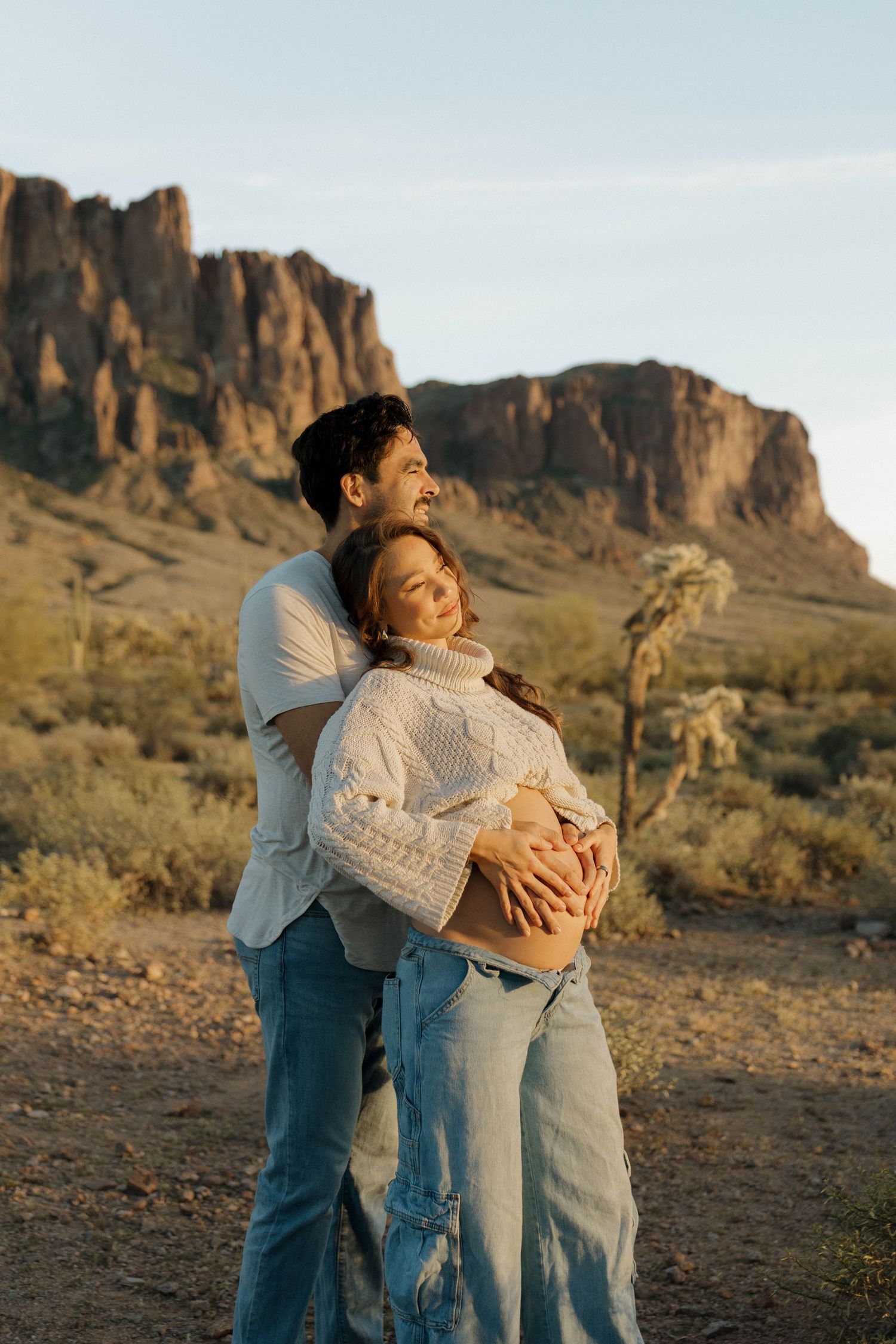 Desert maternity photos with scenic mountain landscape and couple in matching white and denim outfits.