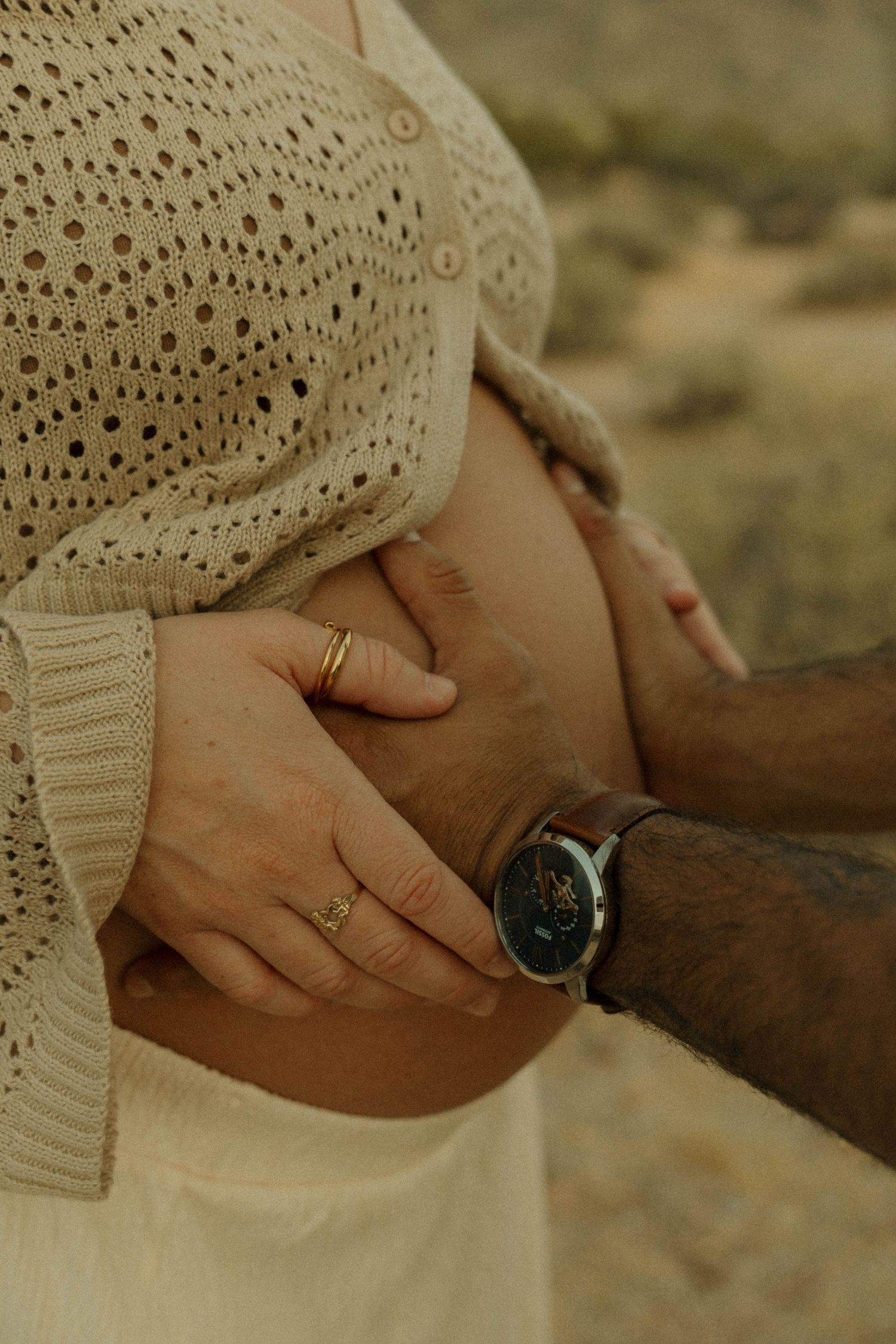 Close-up of couple's hands cradling pregnant belly, man wearing a black watch.