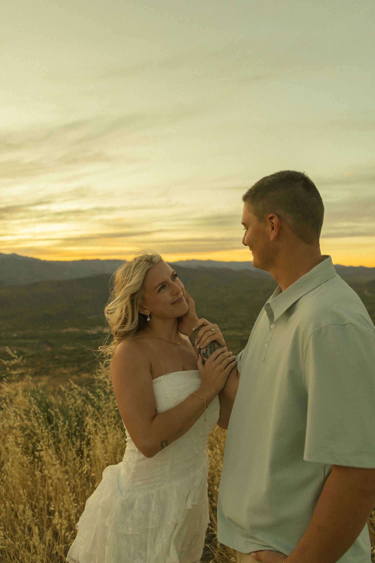 Couple sharing a romantic moment at golden hour sunset with mountains and golden fields in the background.