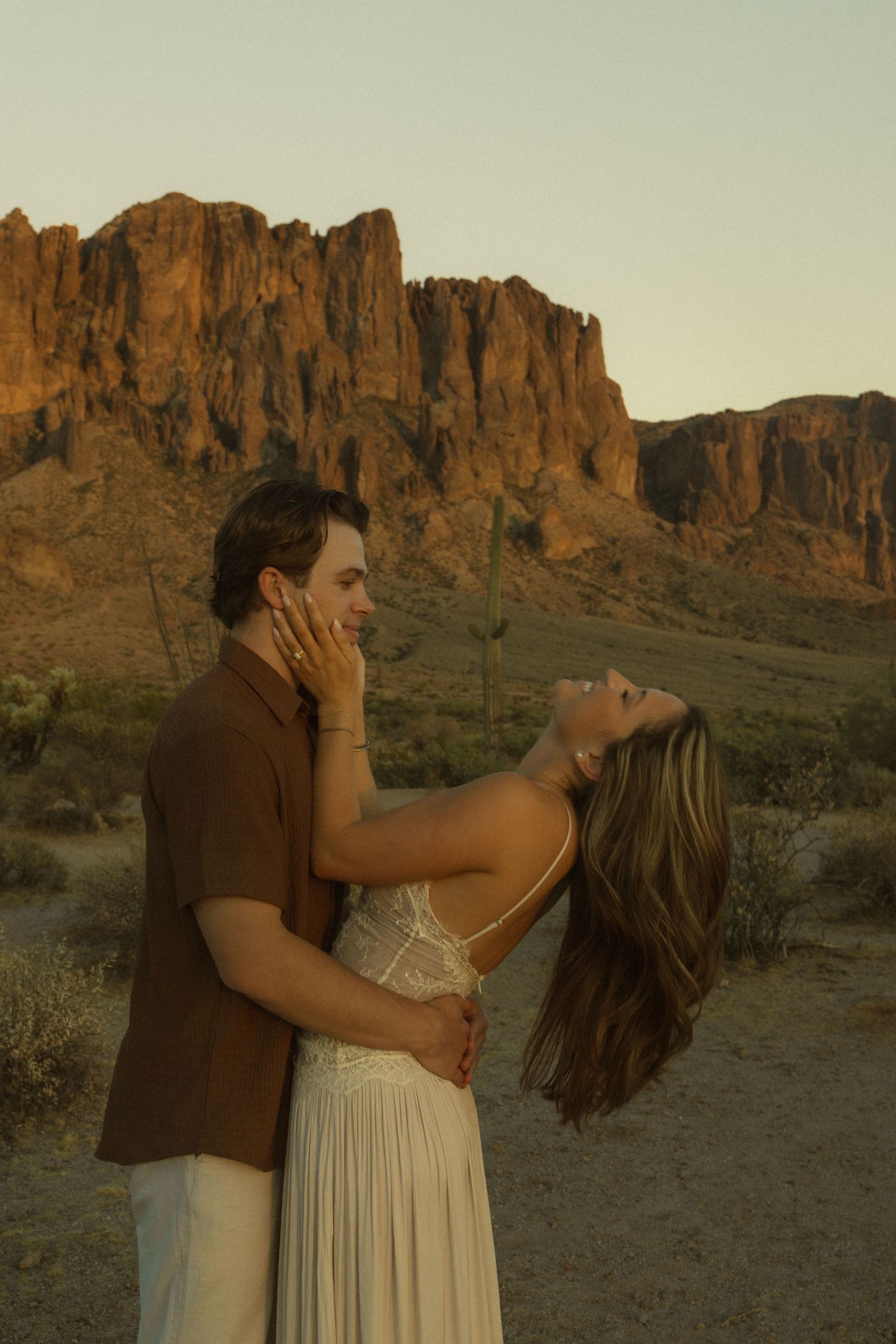 Couple embracing at golden hour in Arizona desert with Superstition Mountains glowing in the background.