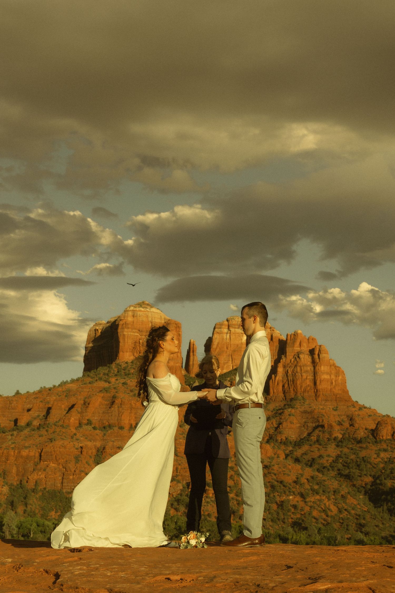 Couple exchanges vows at sunset with Cathedral Rock in Sedona, Arizona as a dramatic backdrop during outdoor wedding ceremony.