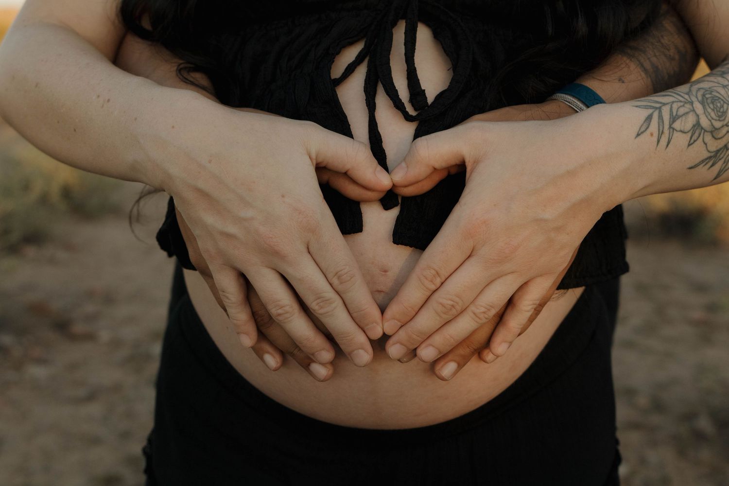 Close-up view of hands holding each other tenderly against a warm sunset background.