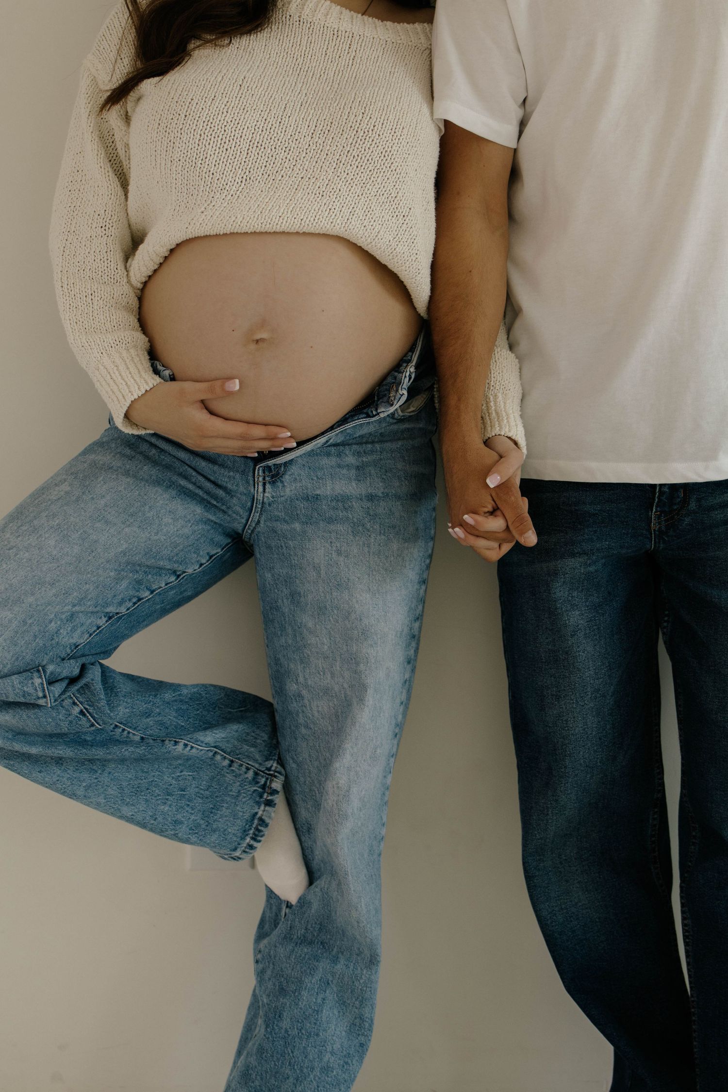 A series of photos showing a pregnancy progression timeline with someone wearing jeans and a white top.