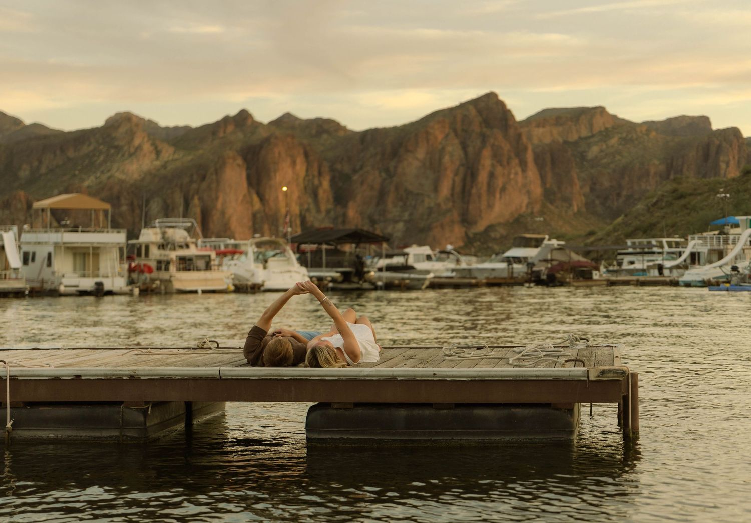 Panoramic view of boats anchored in a harbor surrounded by rugged mountain cliffs at sunset.