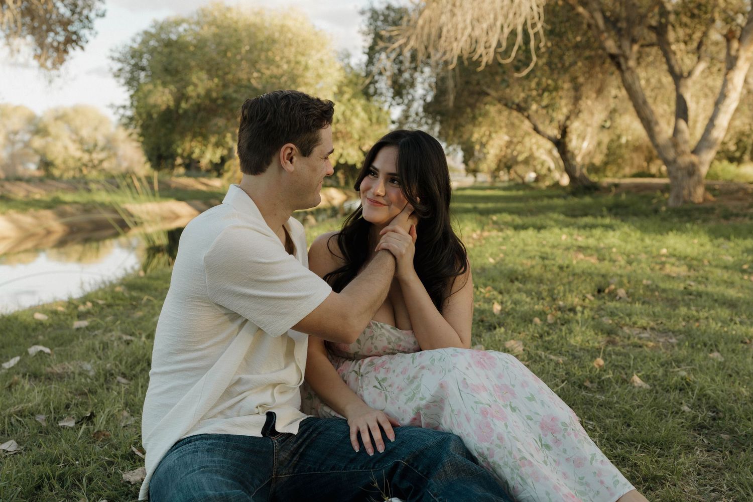 Romantic couple shares tender moment together on grassy hill during golden hour in nature setting.