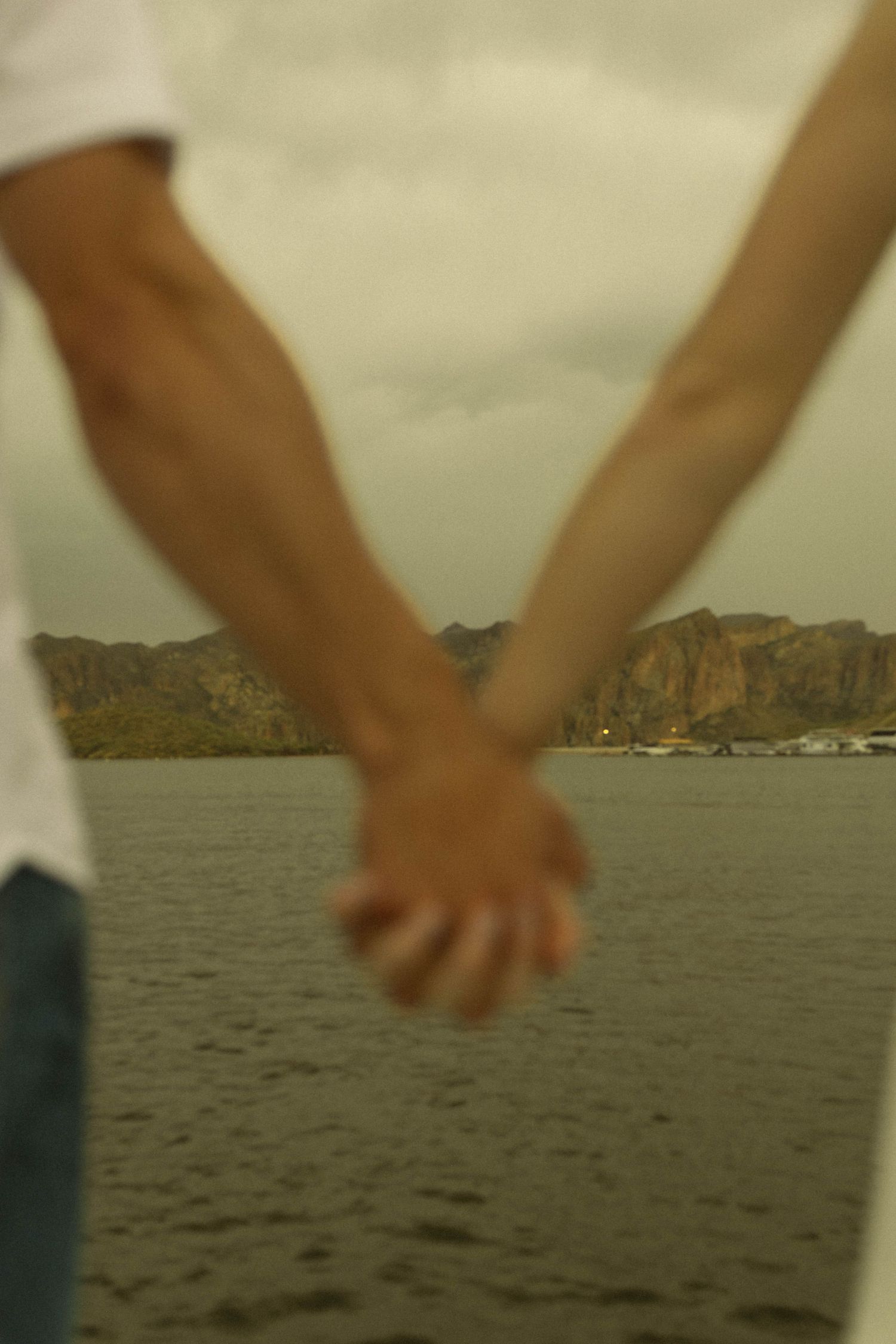 Close-up of clasped hands with scenic coastal cliffs in the background.