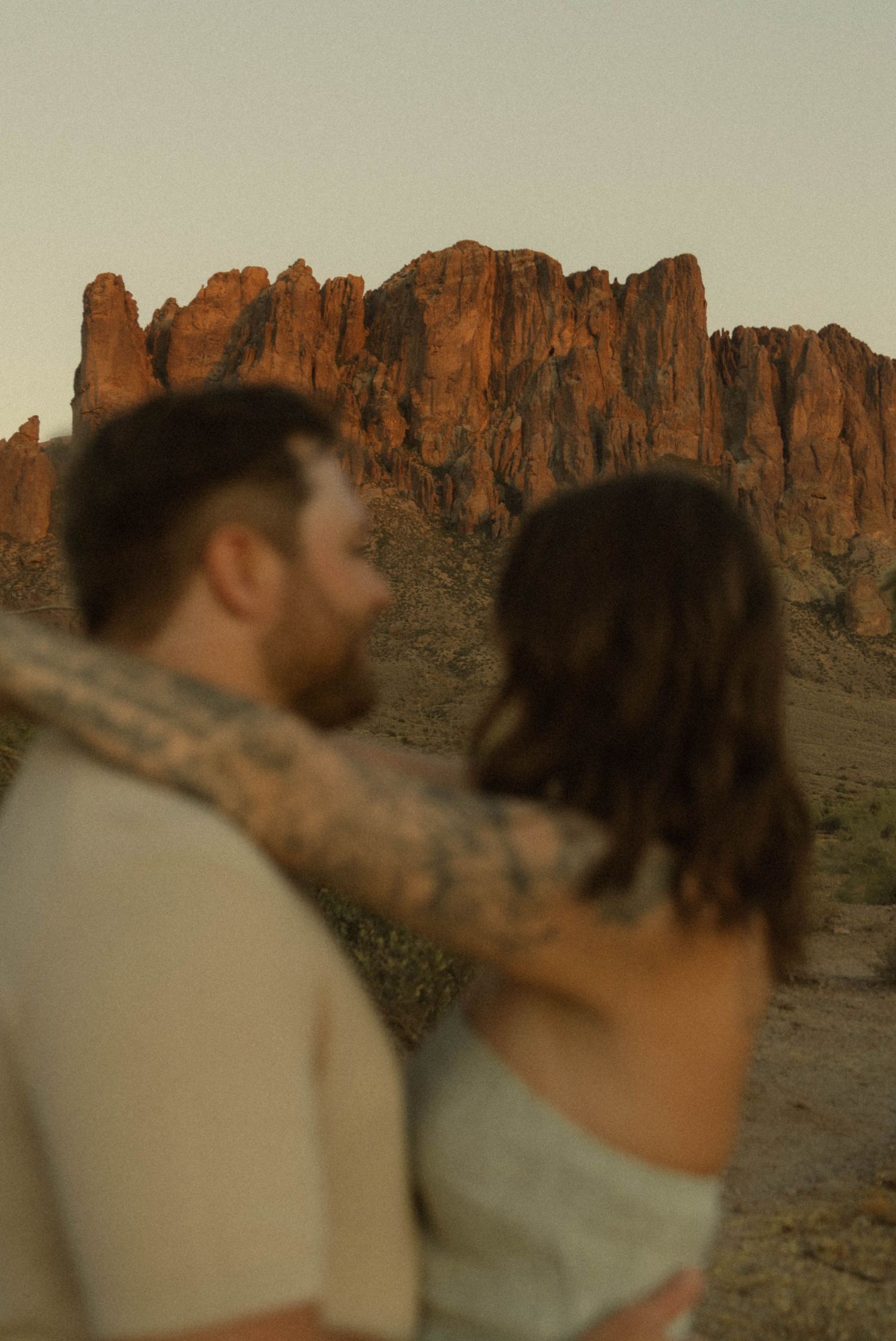 A couple embraces while gazing at the red rock Superstition Mountains in Arizona during golden hour.