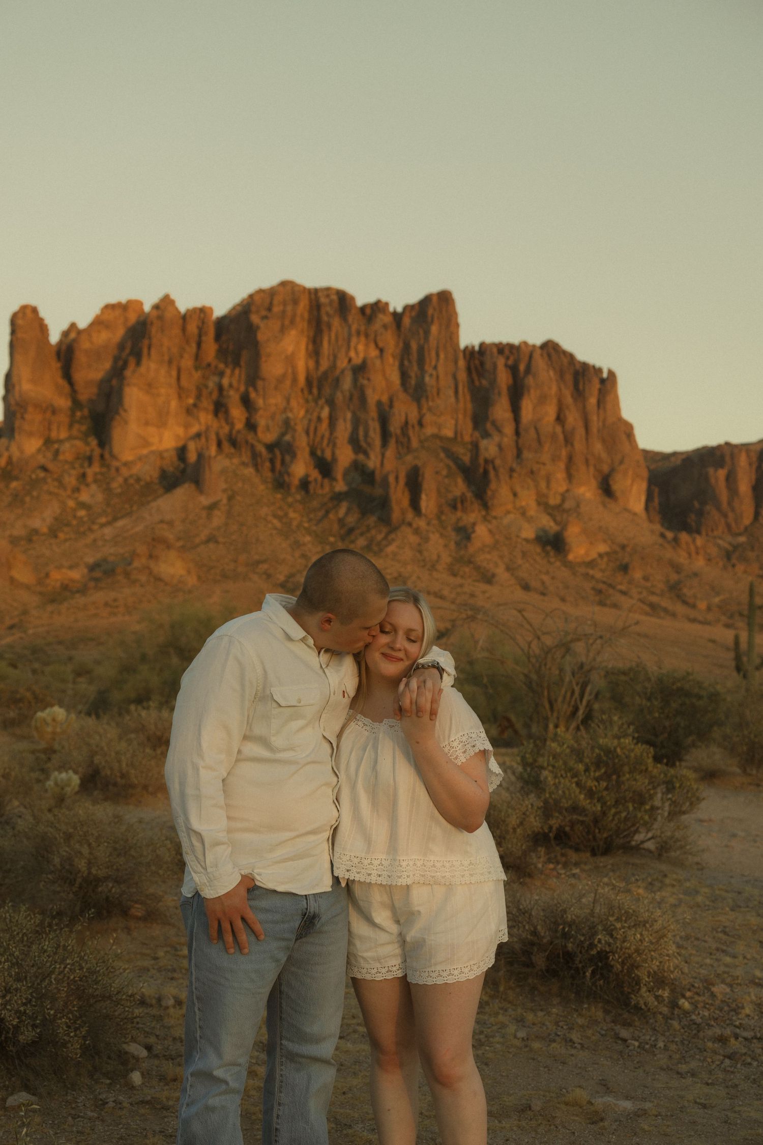 Couple embracing at golden hour with Superstition Mountains in the Arizona desert background.