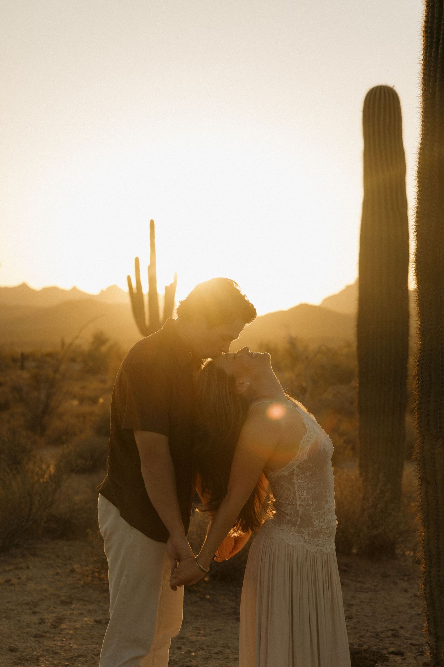 Couple holding hands at golden sunset in Arizona desert with saguaro cacti, romantic engagement photo.