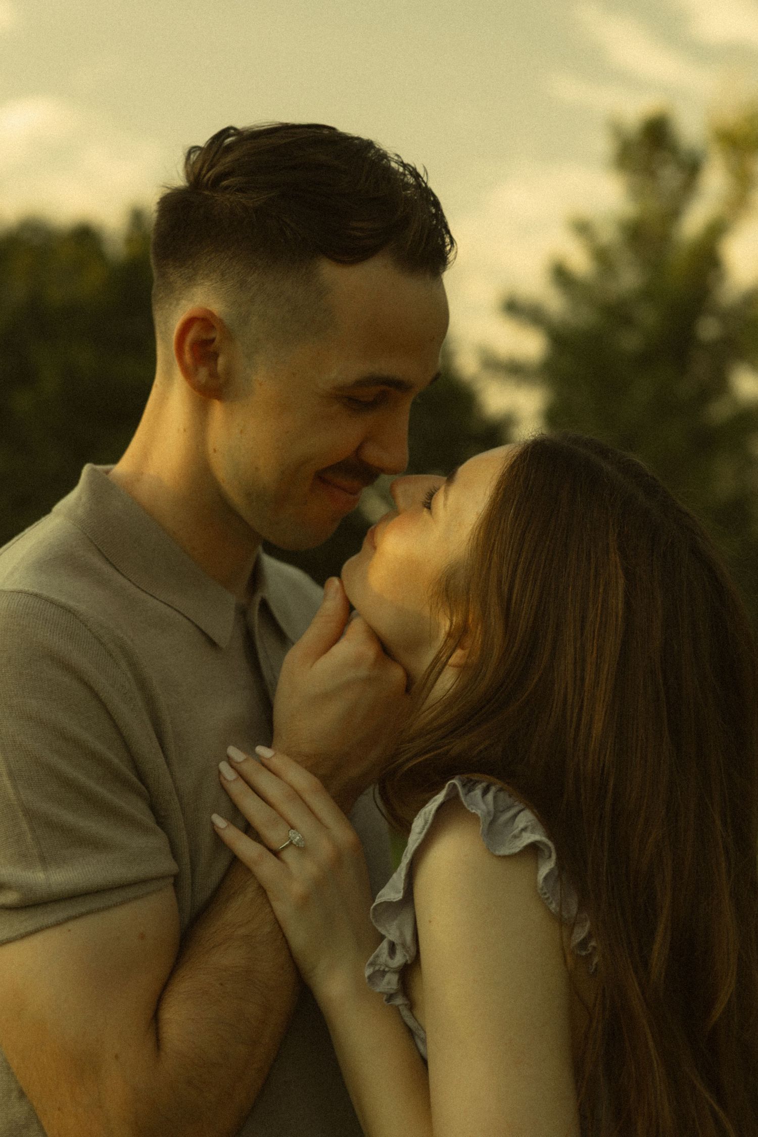 Romantic couple sharing an intimate moment outdoors, smiling and nearly kissing at golden hour.