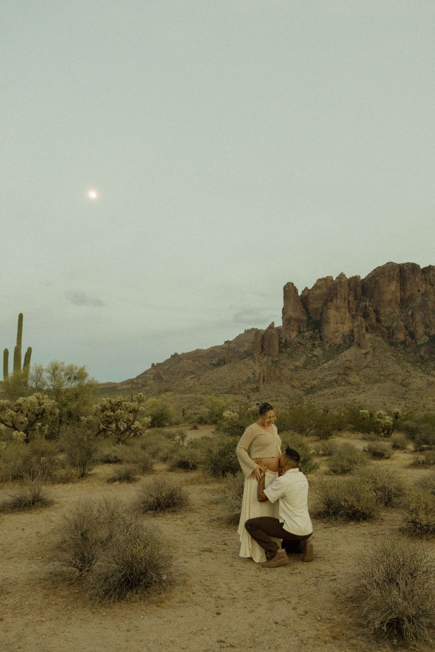 Partner kneeling before pregnant woman in vast Arizona desert under moonlit sky.