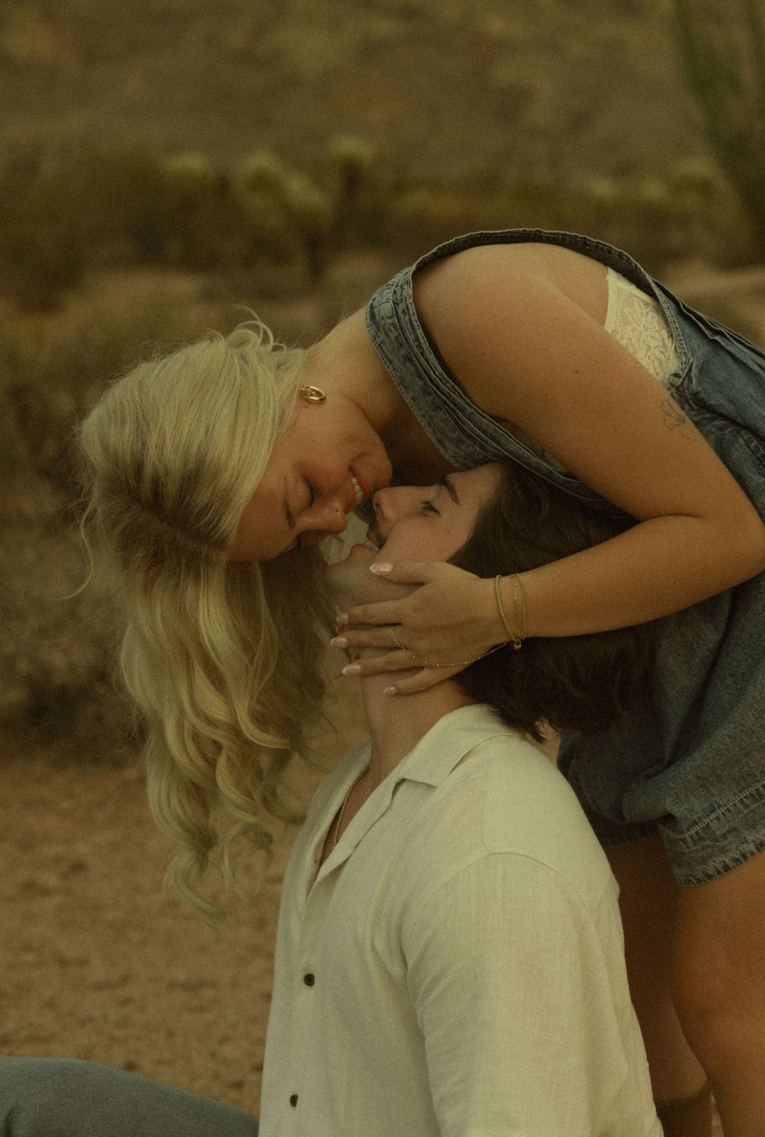 Couple sharing romantic kiss outdoors in Arizona desert with cactus in background.