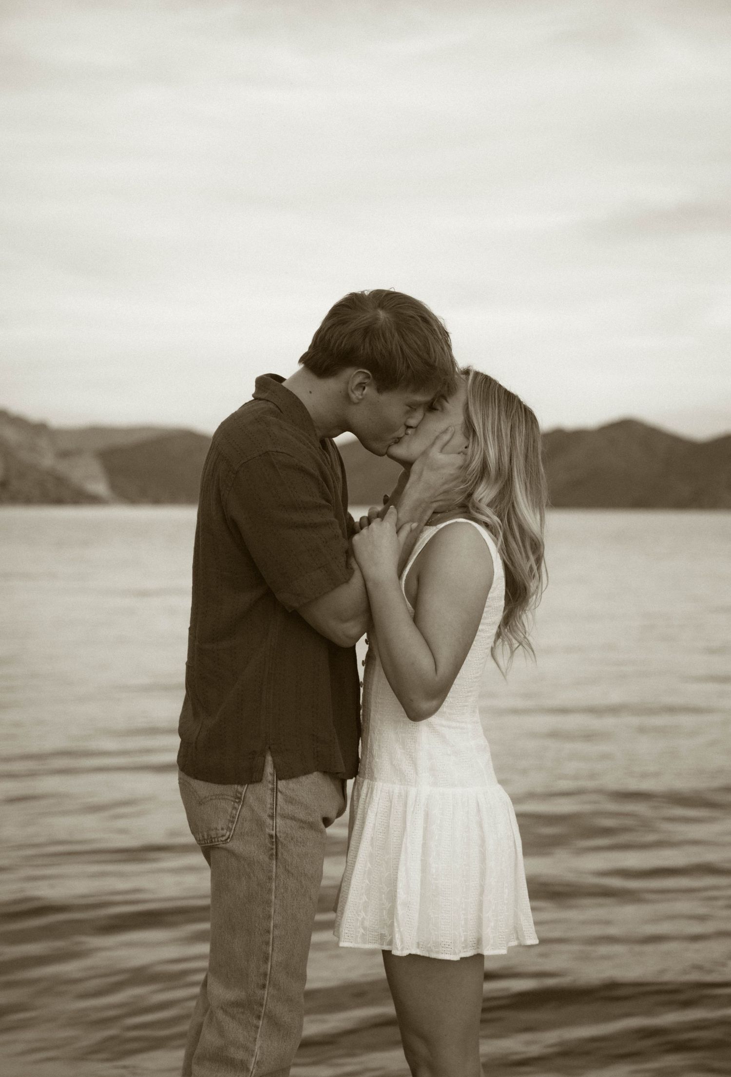 A romantic black and white photo sequence of a couple sharing a tender kiss by a serene lake at sunset.