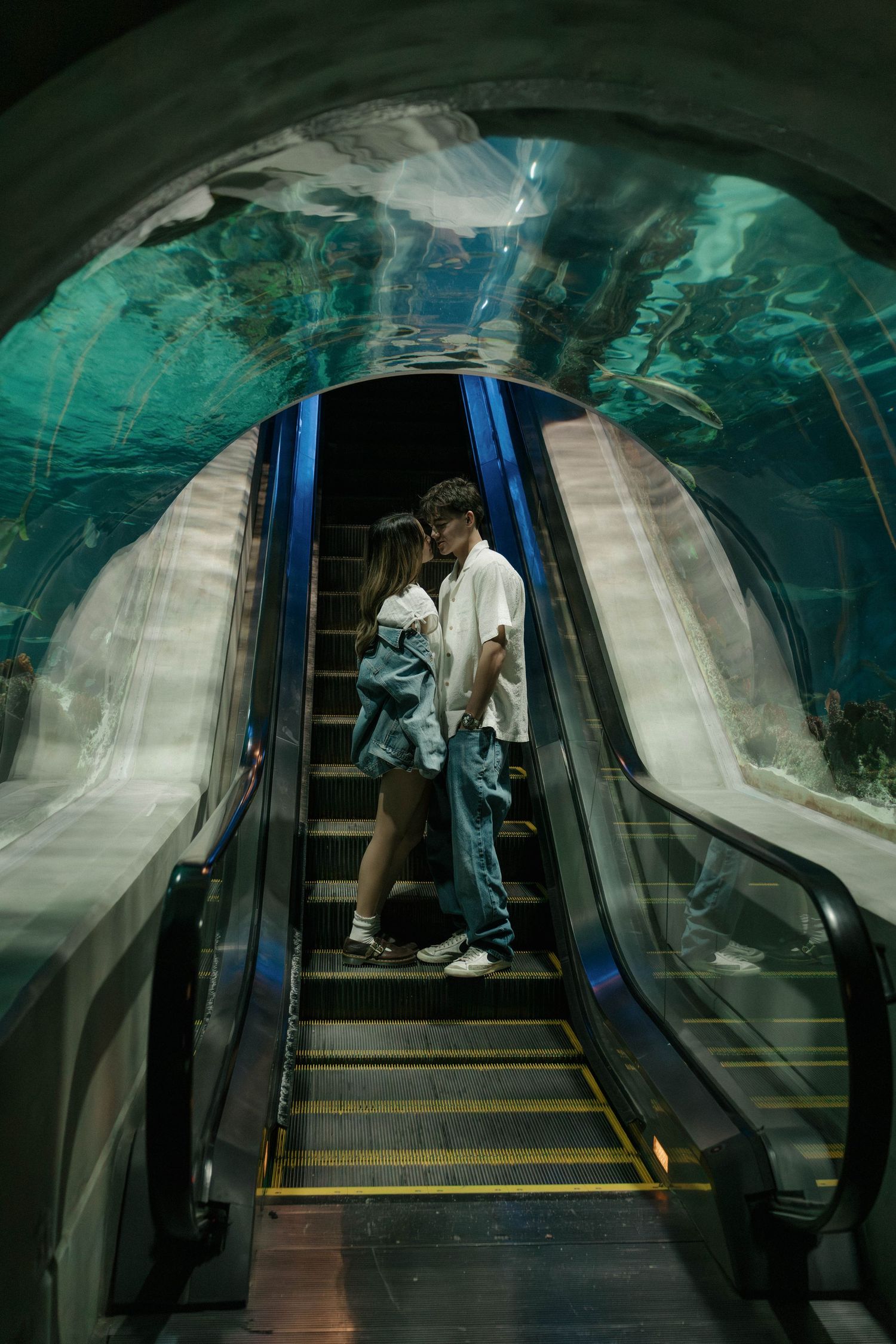 A dark escalator tunnel with turquoise lighting creates a moody atmosphere.