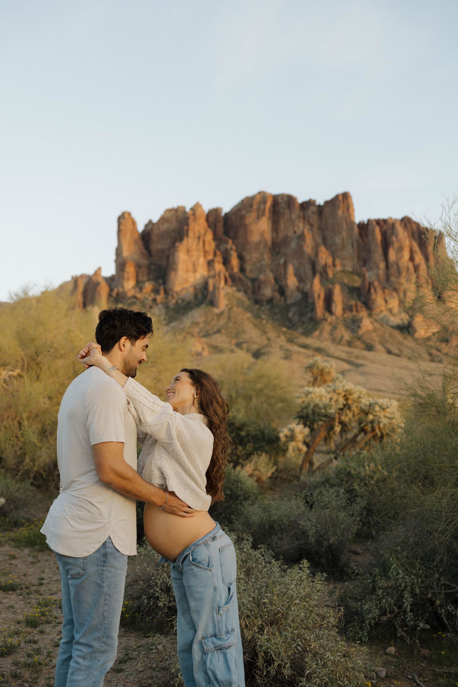 A loving couple shares intimate moments in front of dramatic desert rock formations at sunset.