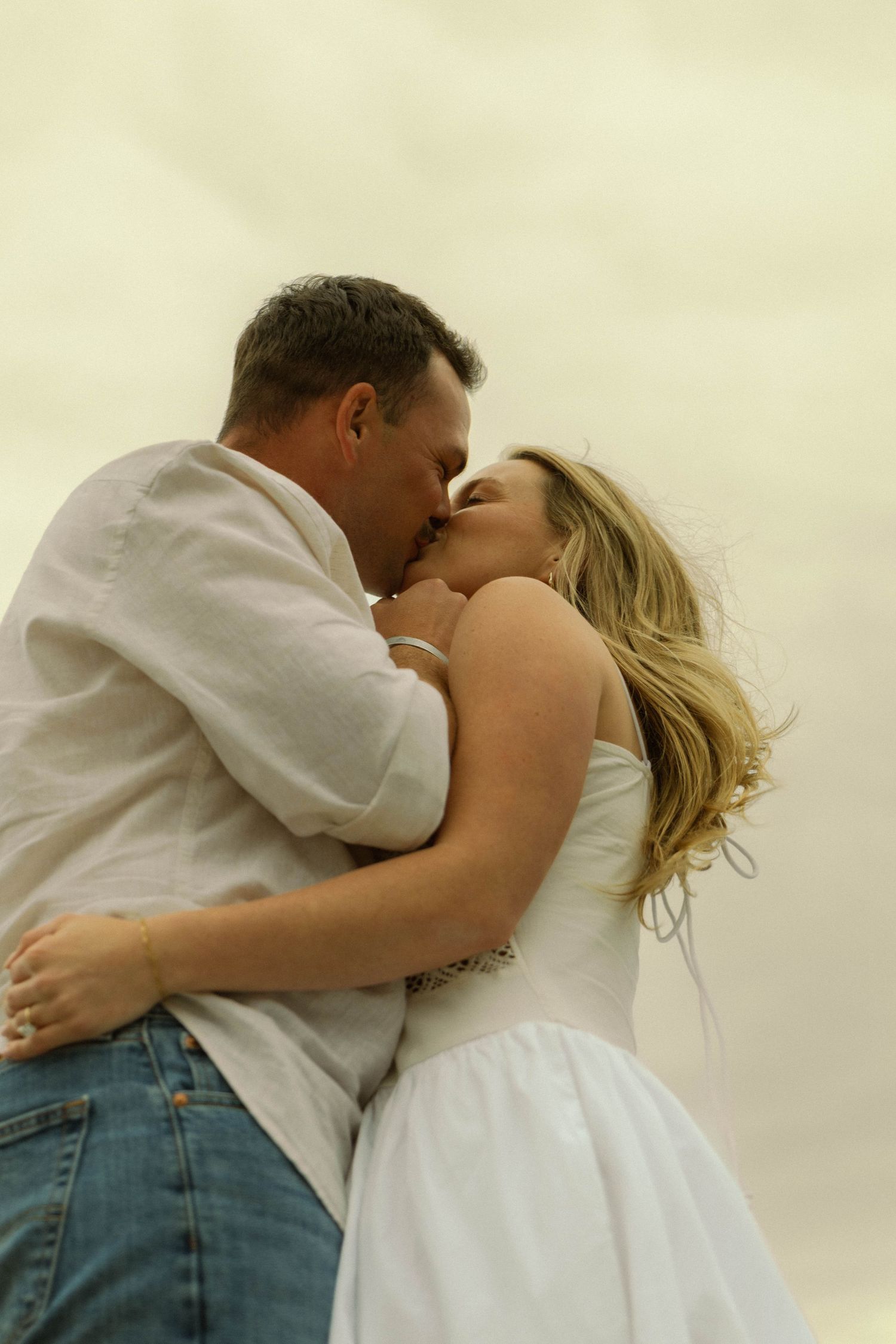 Tender moment between couple in casual attire by water at sunset.