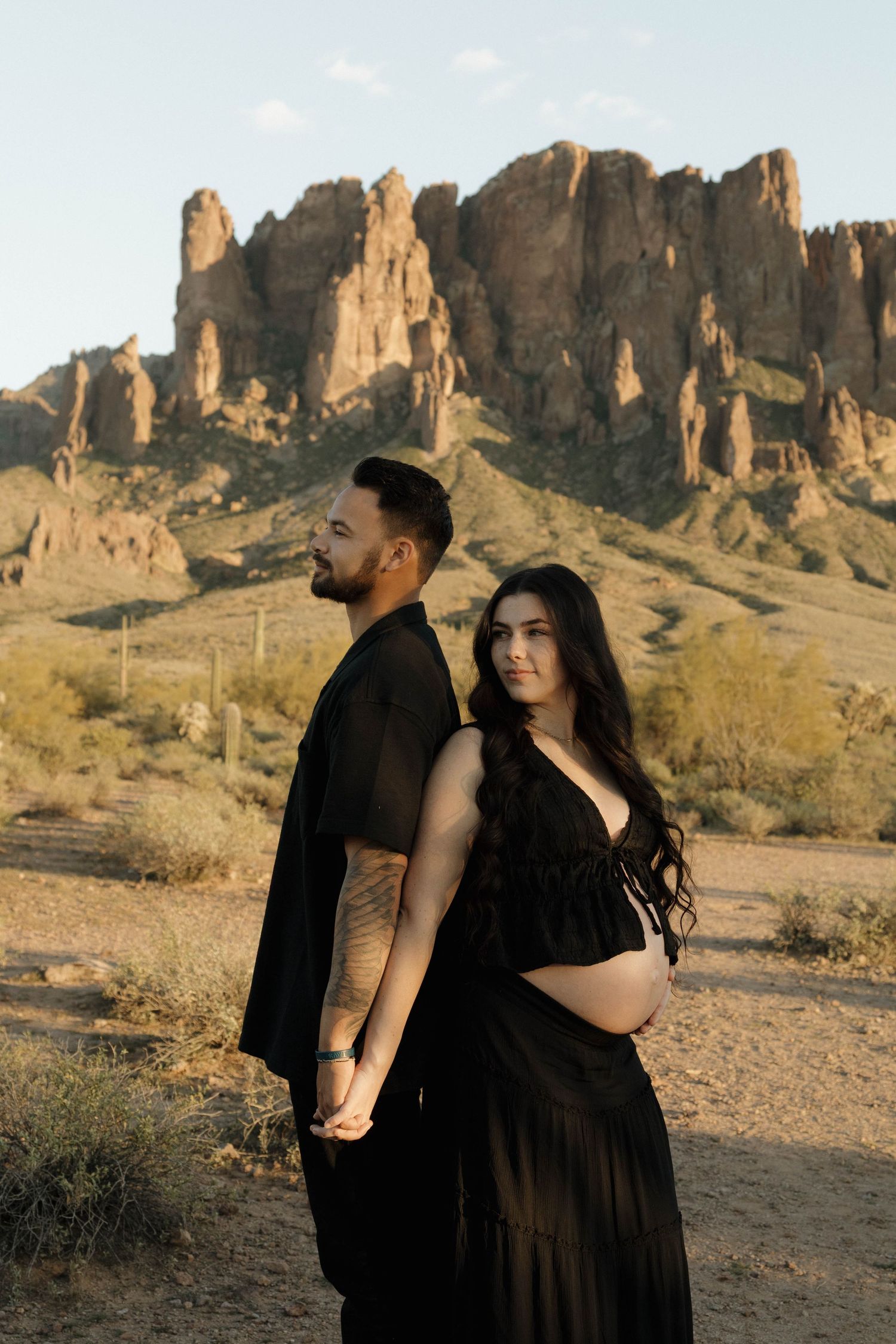 A couple in black outfits embraces in front of dramatic desert rock formations during a photoshoot.