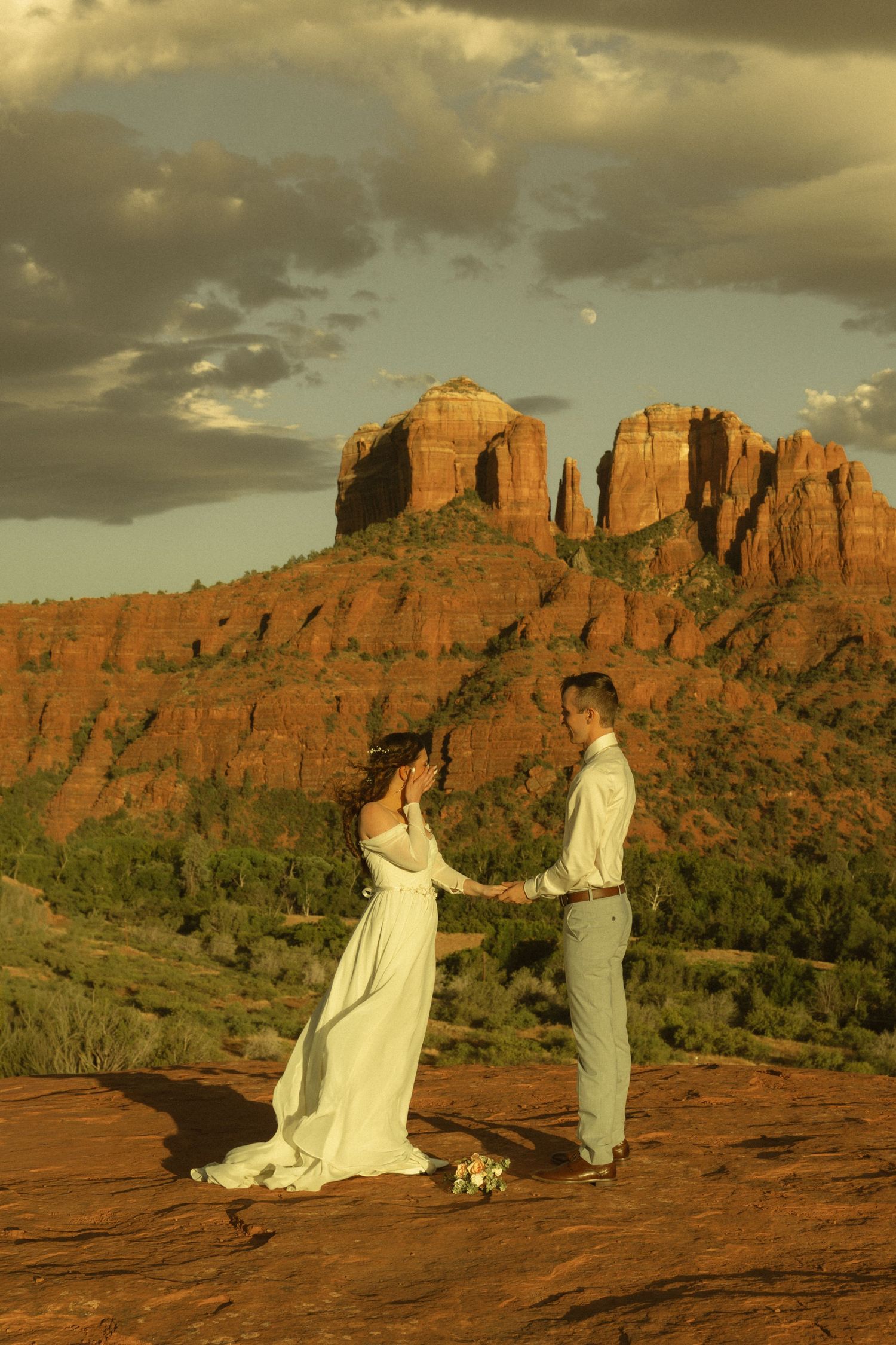 Couple exchanging vows at sunset on red rock formation in Sedona, Arizona, with Cathedral Rock in the background.