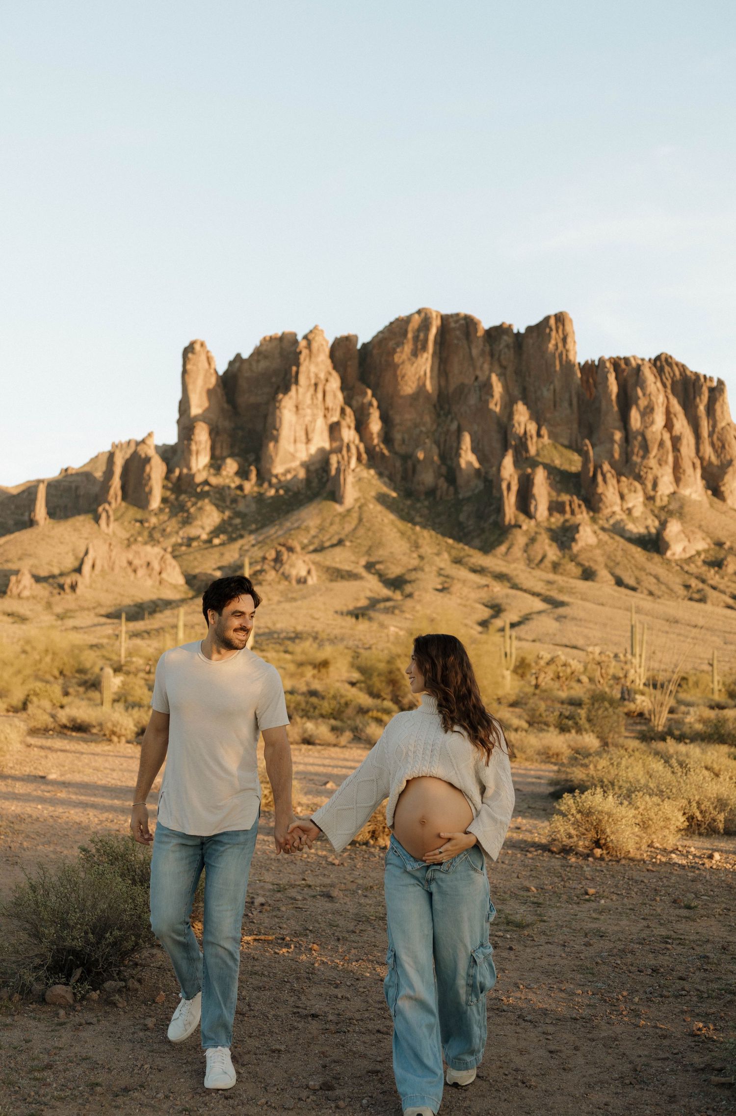 A couple walks hand in hand through a desert landscape with towering rock formations.