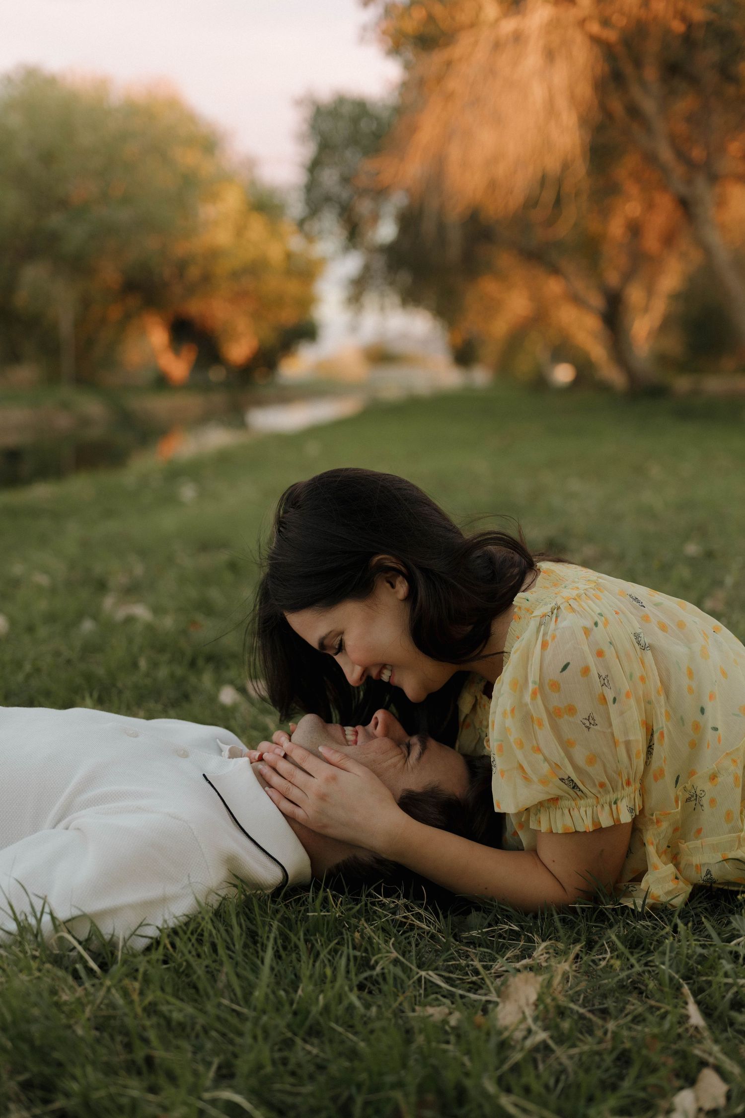 Person in yellow dress lying peacefully on grass during golden hour in a dreamy outdoor setting.