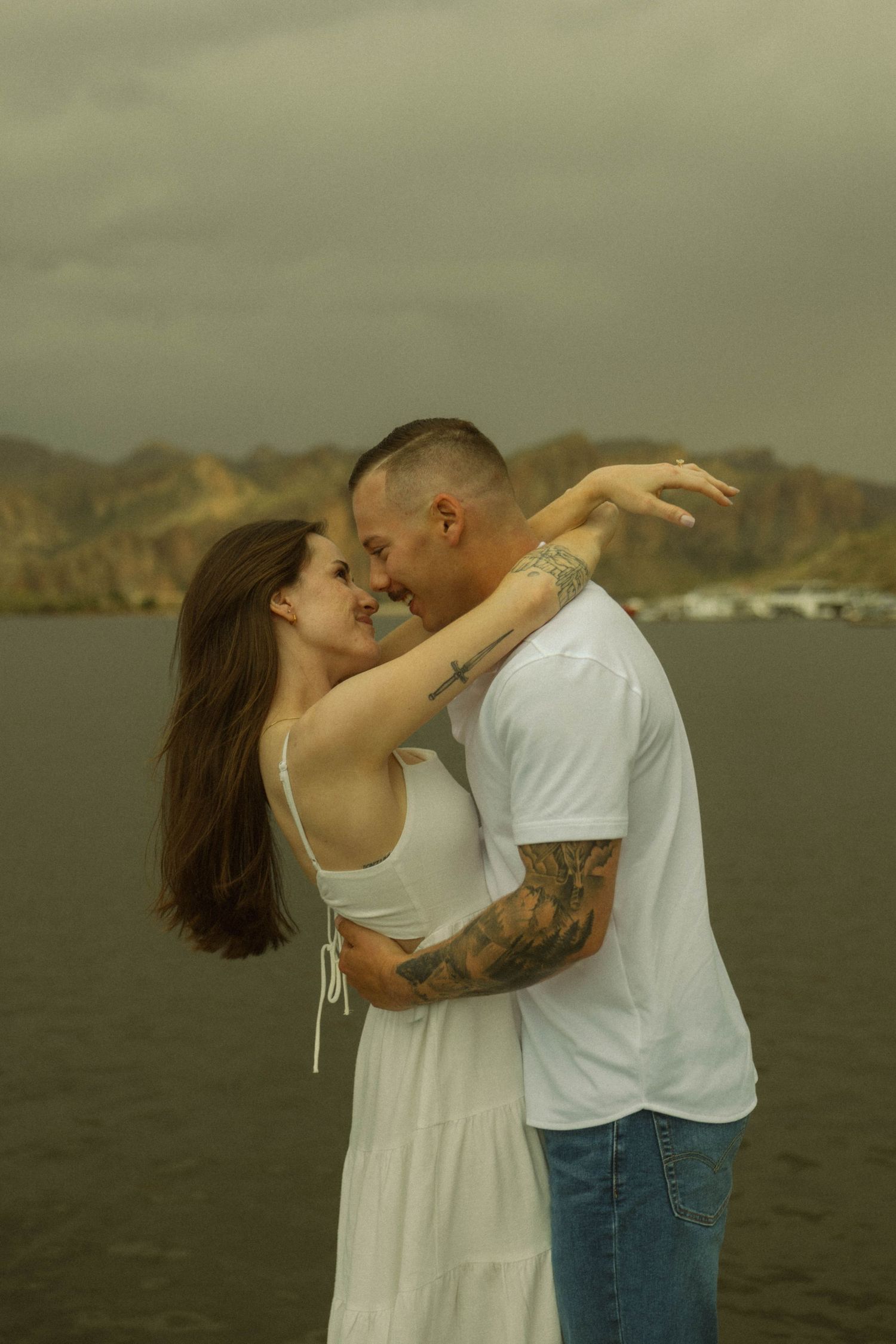 Couple in white sharing a romantic moment against mountainous landscape.