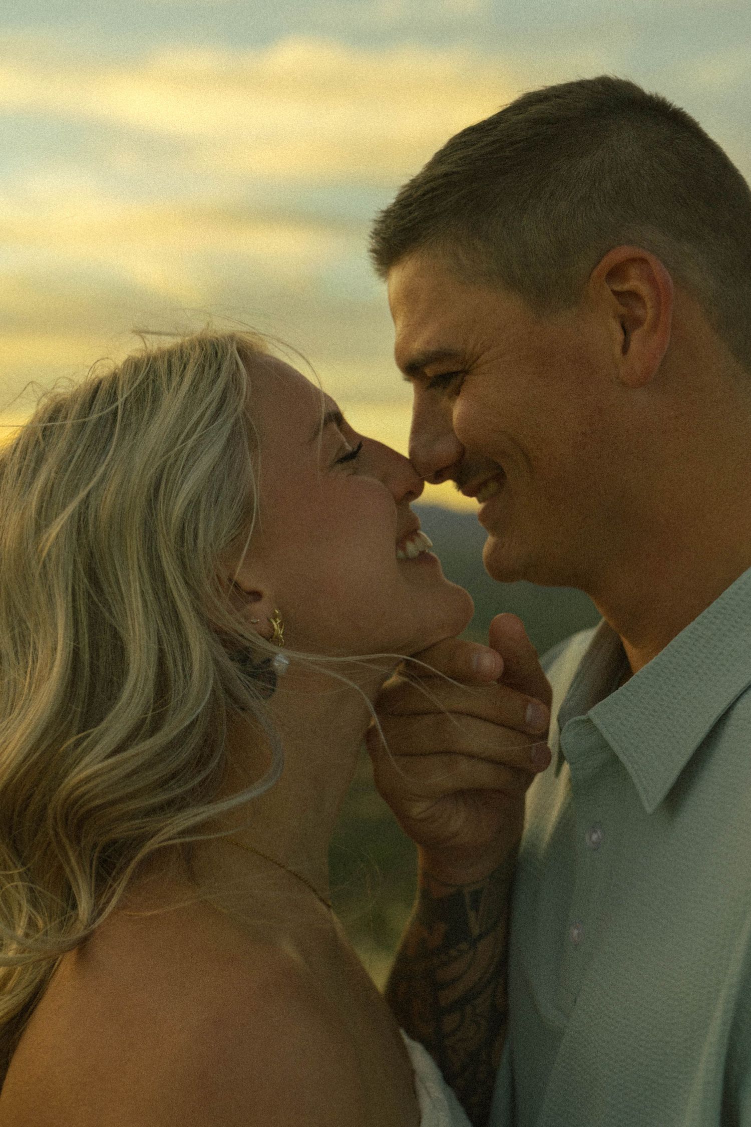 Smiling couple leaning in for a kiss during a warm golden sunset engagement photo session.