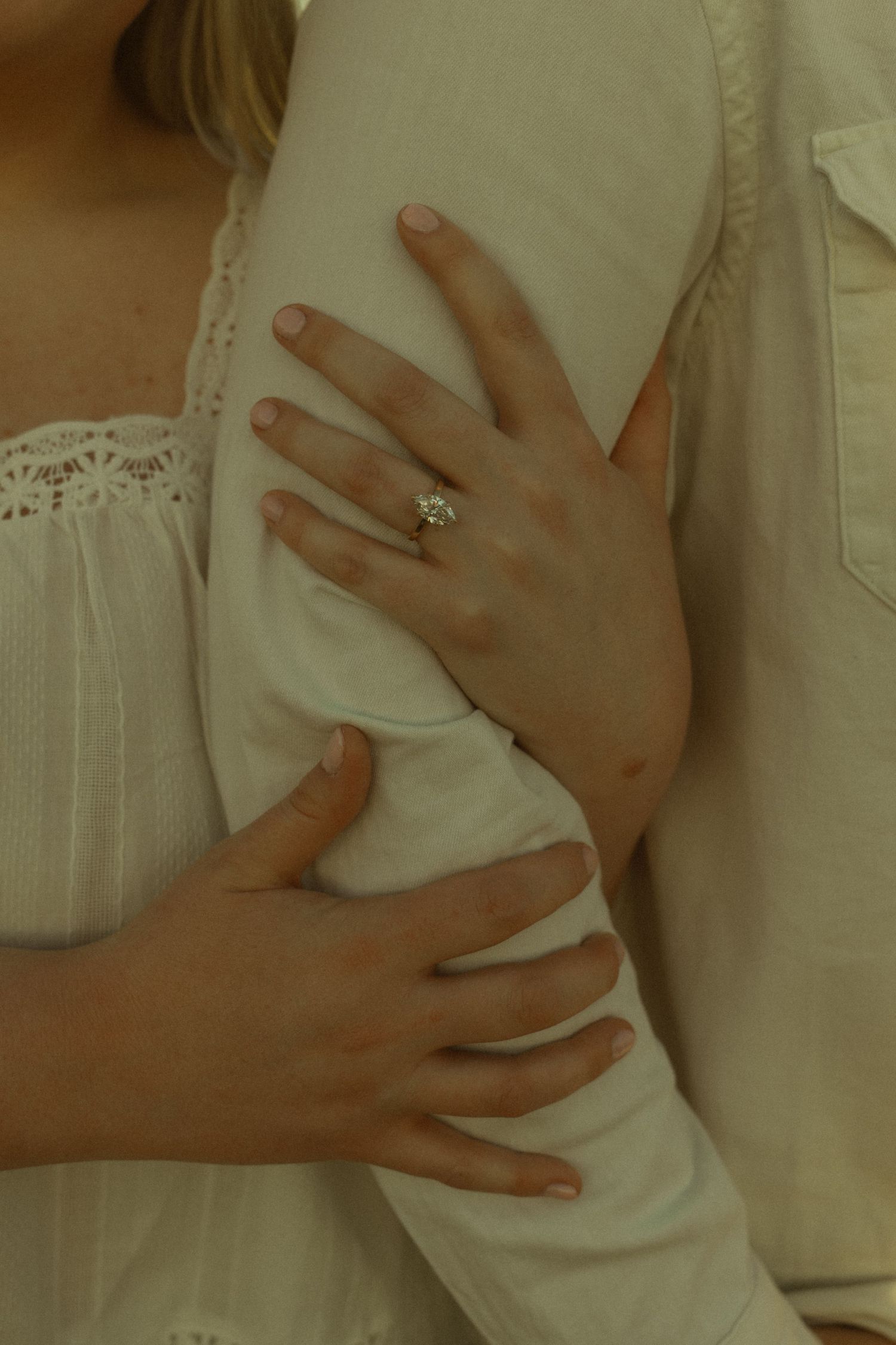 Close-up of a couple embracing, woman wearing a diamond engagement ring on her finger.