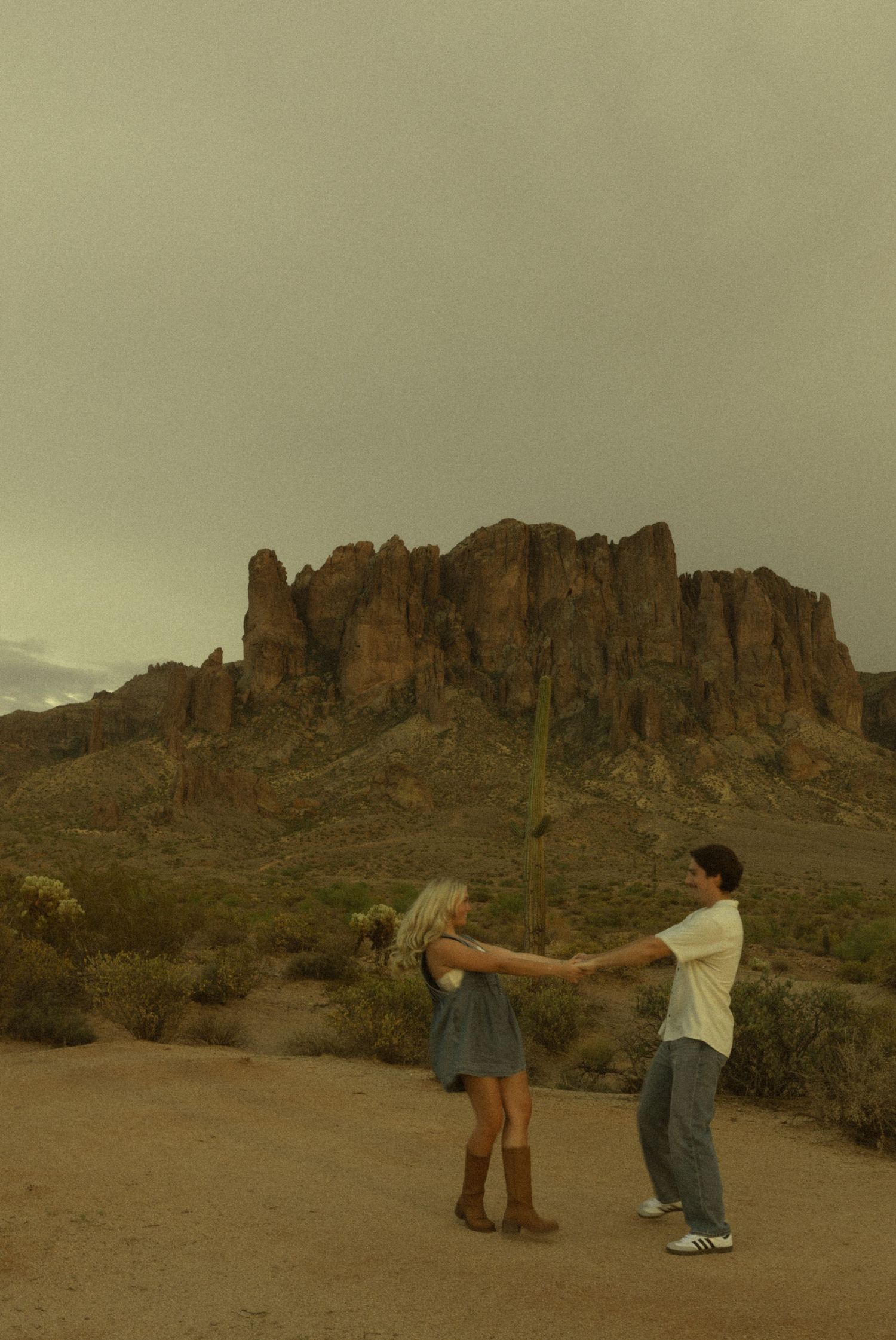 Couple dancing together on desert path with dramatic Superstition Mountains behind them.