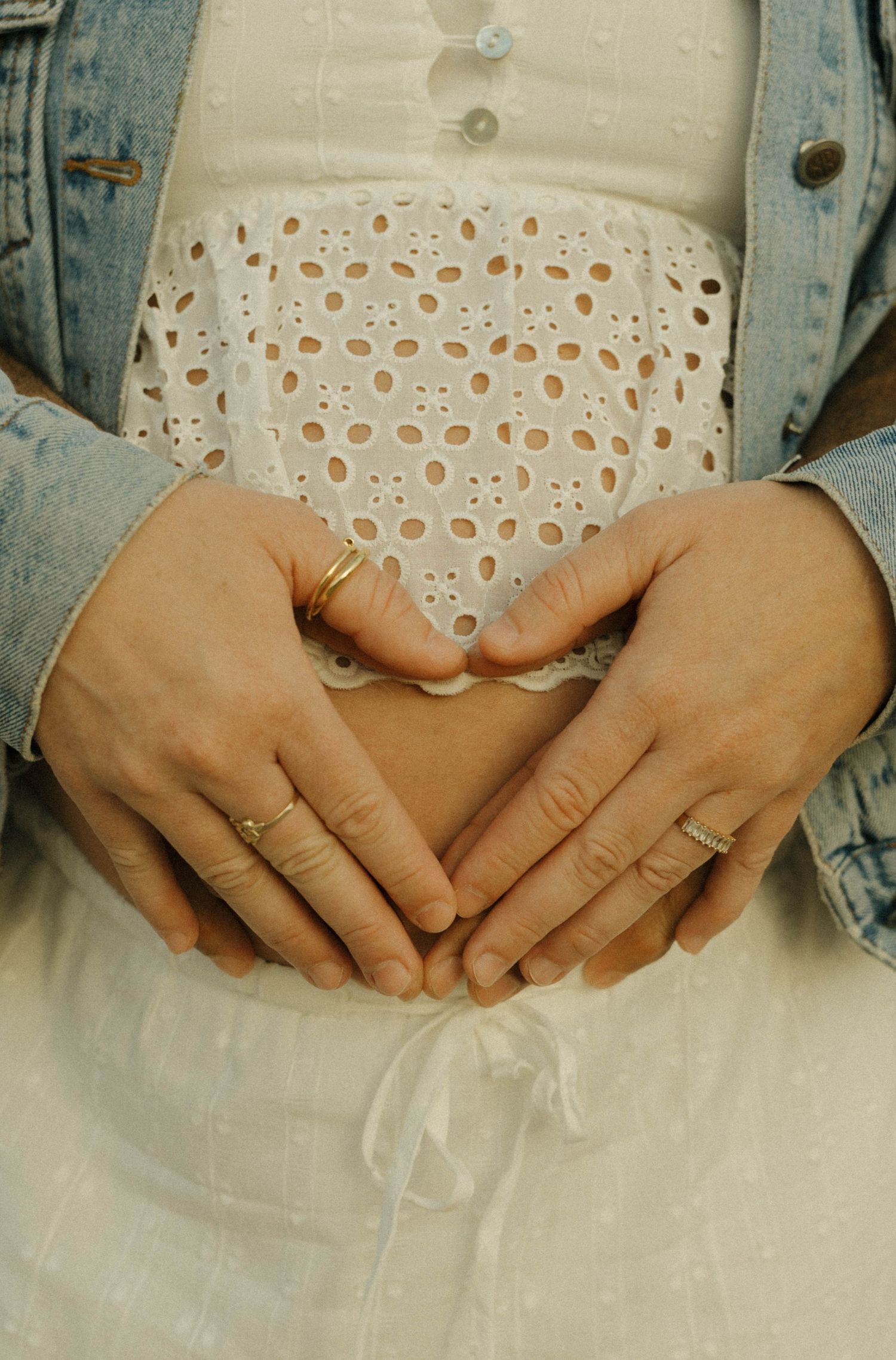 Pregnant woman and partner form heart shape with hands on baby bump.