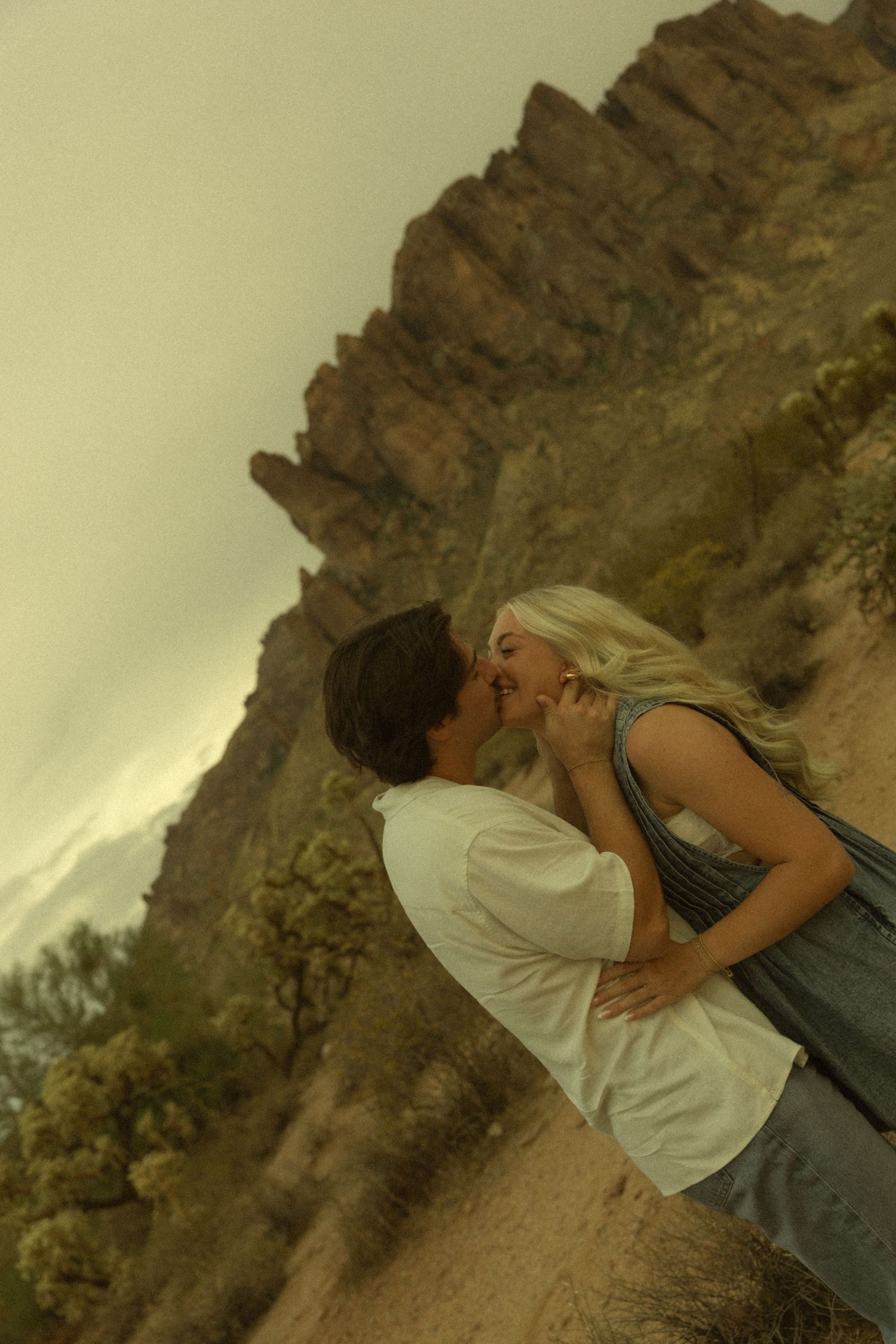 Romantic couple sharing a kiss against stunning desert canyon landscape during golden hour sunset.