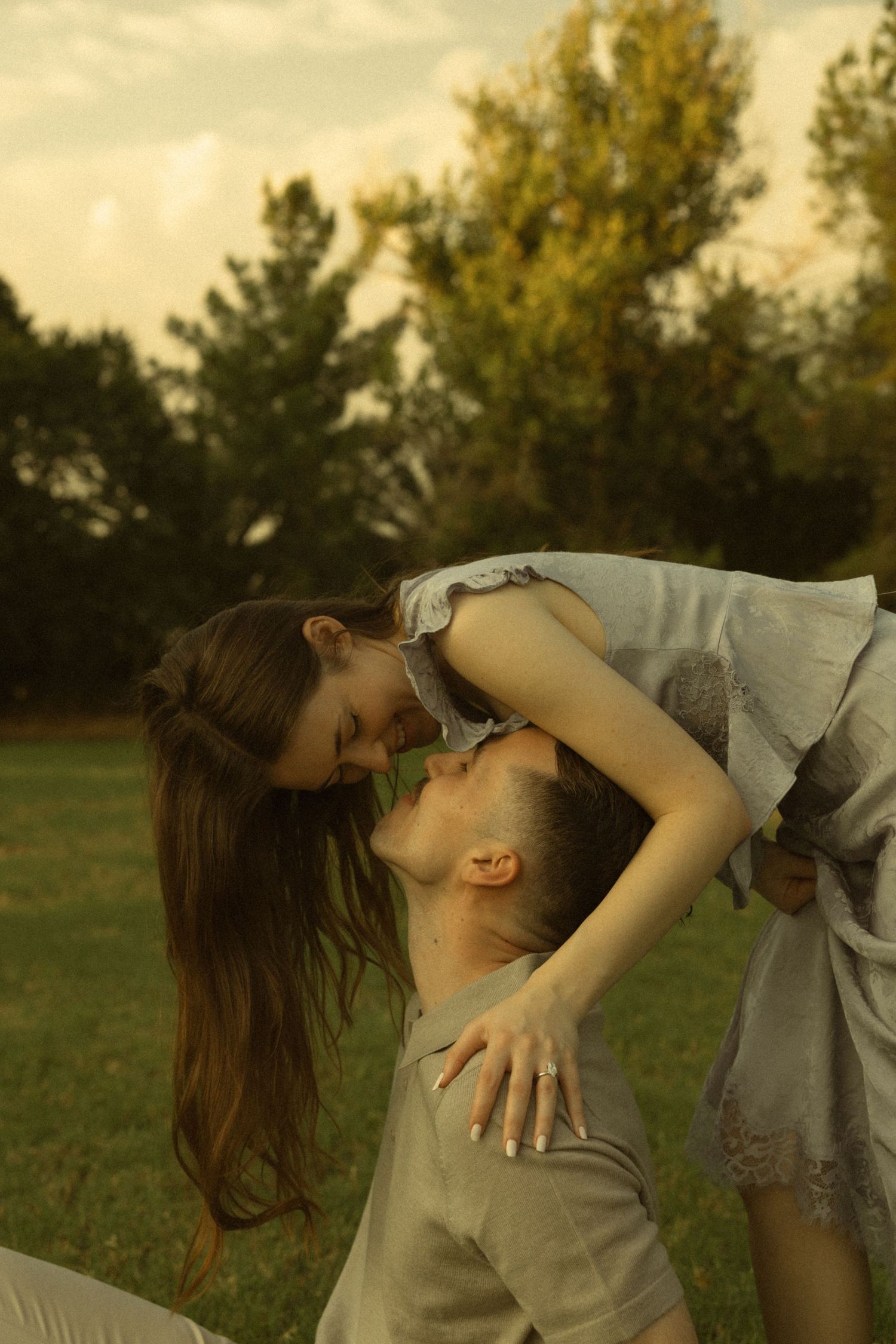 Romantic couple sharing a tender moment outdoors, man lifting woman in a green park setting at golden hour.