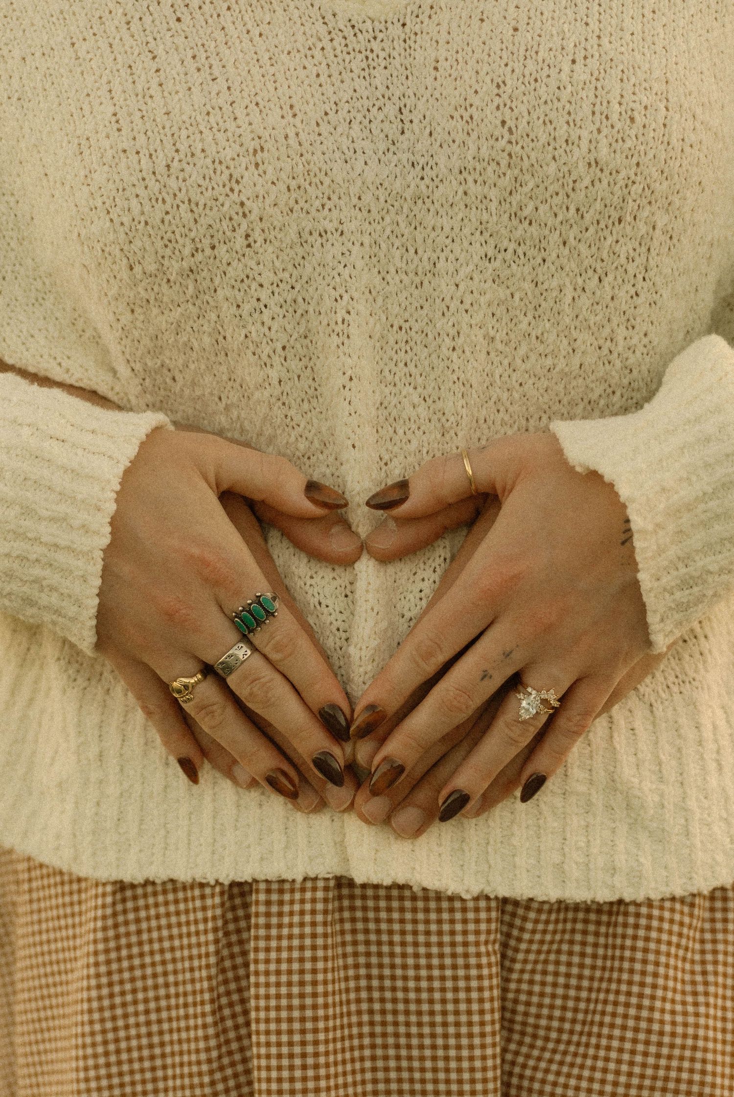 A series of hands wearing a diamond ring shown against a cream sweater and gingham fabric background.